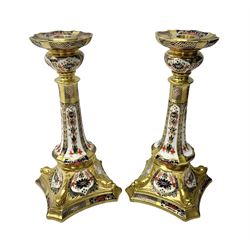Pair of modern Royal Crown Derby Old Imari 1128 pattern candlesticks, each with shaped drip tray affixed to squat socket, upon spreading stem and canted square base with gilt dolphin edges, with printed marks beneath including Roman numeral year cypher for 2003, H26.5cm, with original boxes