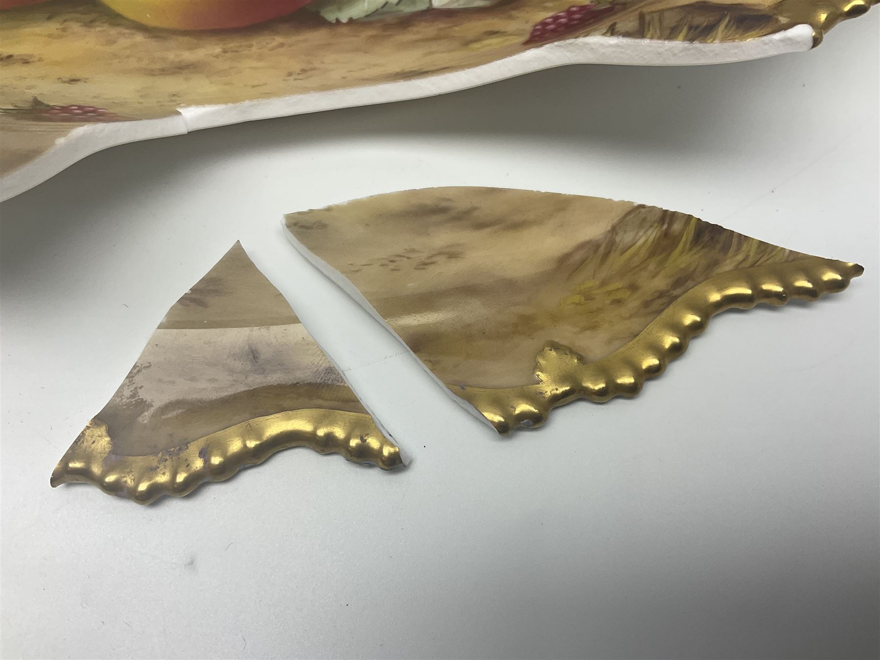 Early 20th century Royal Worcester dish decorated by Thomas Lockyer, oval form with gilt shaped rim and twin shell handles, hand painted with a still life of fruit upon a mossy ground, signed T Lockyer, with puce printed mark beneath and date code for 1922, for restoration, W31cm