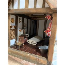 Gerry Welch for Manorcraft Tudor style wooden doll's house, of three-storey multi gabled form with mock beam and plaster walls and simulated leaded glass windows under a felt tiled roof, boarded floors and stairs to each room, curtains to most windows, front entrance door, rear door and single storey extension for kitchen. Furniture includes fitted floral bathroom suite to top floor, well stocked Welsh dresser with copperware etc, tapestry style wall hangings, knole settee, tin bath, metal range, fire-surround, wooden three-piece suite etc; on shaped cobbled base W91cm D61cm H91cm