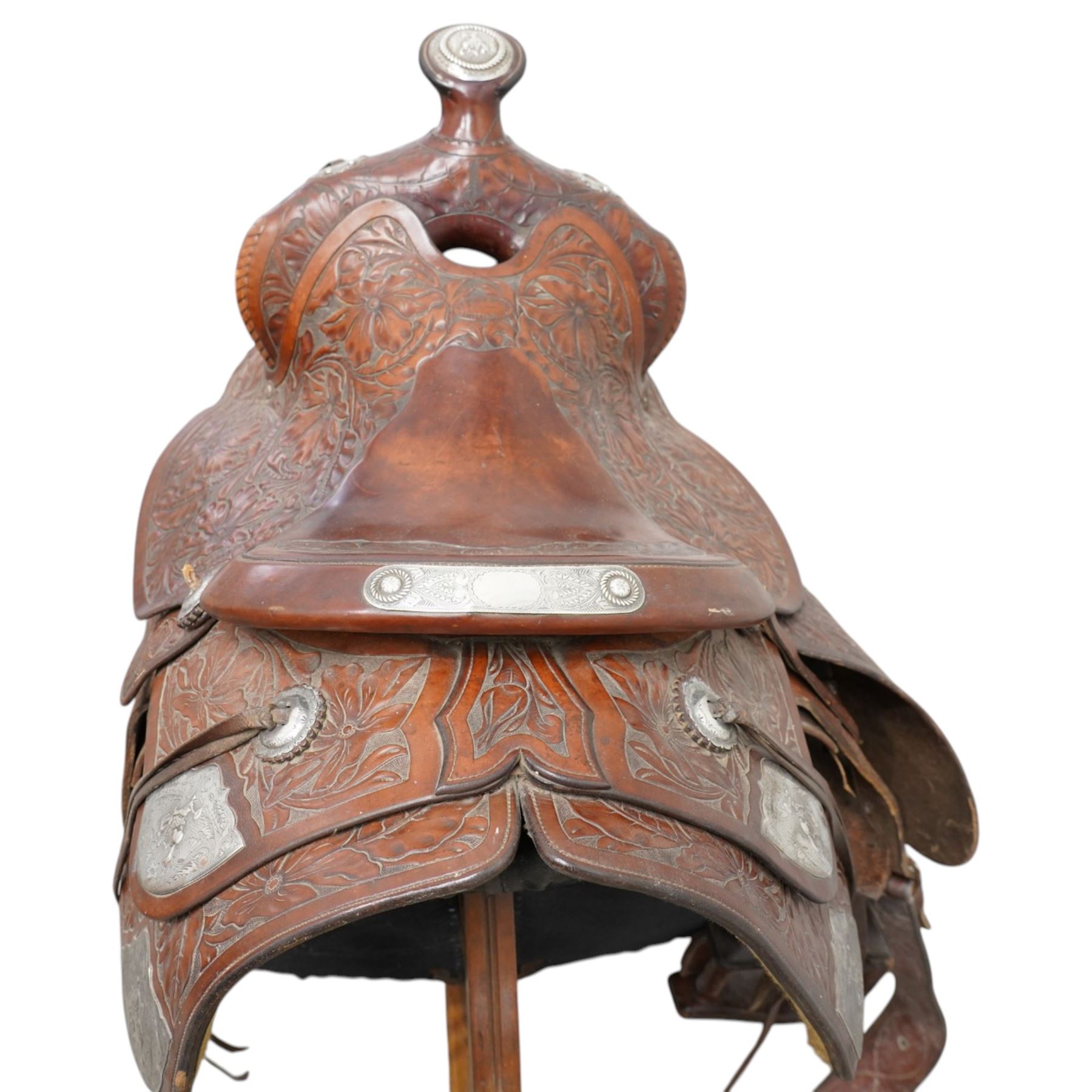 Keyston Bros (San Francisco) - 1930s/1940s 18’ American leather and silver mounted Western Parade saddle, the mahogany-tone leather body heavily hand-carved in a deep California Poppy floral pattern, surmounted by a ‘Bear Trap’ pommel fitted with an oval horn cap featuring a silver medallion of a cowboy on a bucking horse, further embellished with engraved sterling silver mountings, including large domed conchos, full-dress skirt corner plates, and a continuous cantle trim band, together with the associated girth, stirrups and leathers