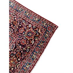Large Persian Kashan crimson ground carpet, large floral central medallion surrounded by trailing branches decorated with leaves and stylised plant motifs, the main border with scrolling design interspersed with palmettes, within floral pattern guard stripes 
