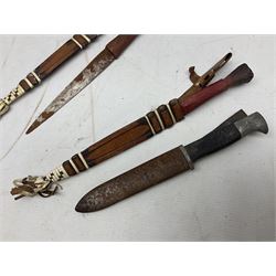 Indian kukri with 29cm curving steel blade and nickel mounted horn grip; in leather covered scabbard with one skinning knife L42cm overall; Hitler Youth knife with scabbard in relic condition; and three African graduated knives each with crudely carved wooden grips and painted leather covered scabbards (5)