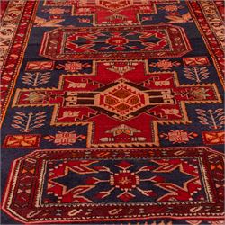 North West Persian runner, the indigo field decorated with three stepped cruciform medallions alternating with two octagonal panels, interspersed with stylised flowerheads and foliage, enclosed by an ivory ground floral border and red guard bands