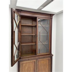 Late Regency mahogany bookcase on cupboard, projecting cornice over two moulded astragal glazed doors, the left-door hinges to allow the right-hand door to slide, central slide over double panelled cupboard, flanked by reeded uprights, on turned a lobe carved feet