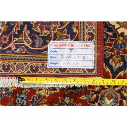 Central Persian Kashan hand-knotted rug, deep red field with central cusped ivory medallion with an all-over arrangement of scrolling floral vines, palmettes and flowering sprays within conforming spandrels, principal navy border with a continuous meandering vine of palmettes and stylized floral motifs, enclosed by multiple narrow guard borders, with cotton fringe ends 