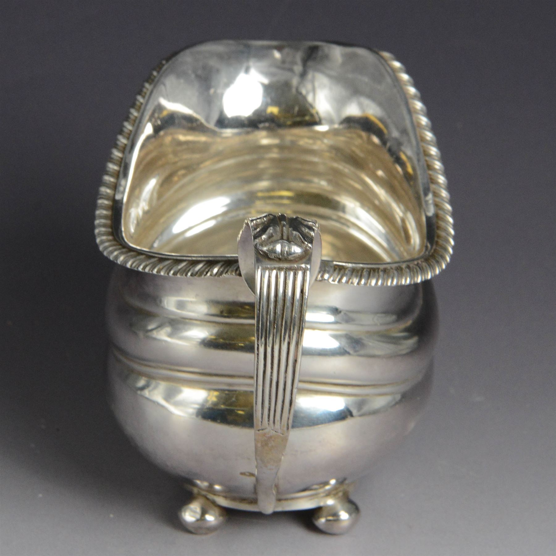 George III silver milk jug, of oval form with oblique gadrooned rim and acanthus leaf capped handle, upon four bun feet, hallmarked London 1819, maker's mark worn and indistinct, H10cm