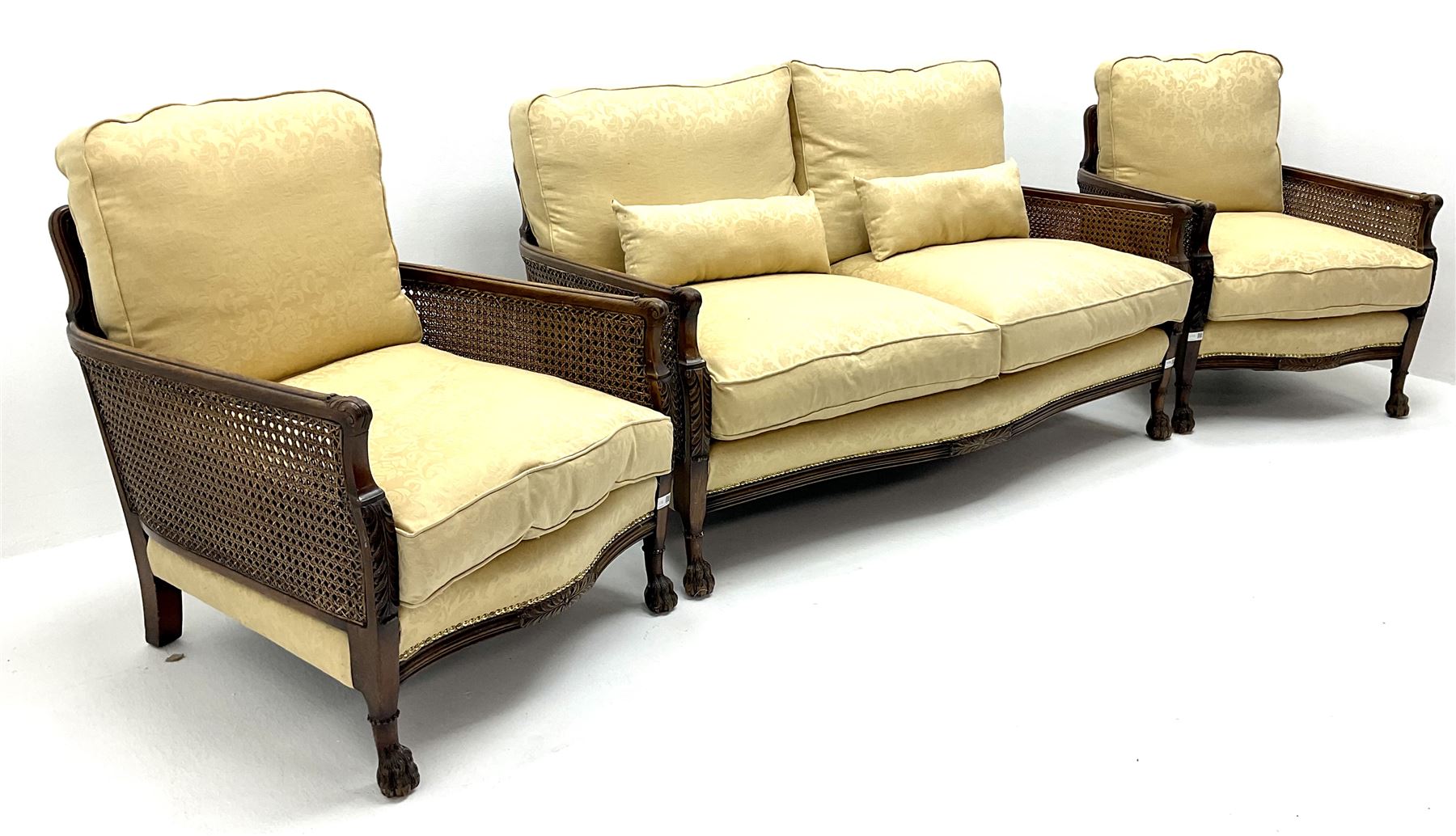 Early 20th century mahogany framed Bergere settee, double cane sides with acanthus carved arms on hairy paw feet, upholstered in a pale gold fabric (W145cm) and two matching armchairs (W66cm)