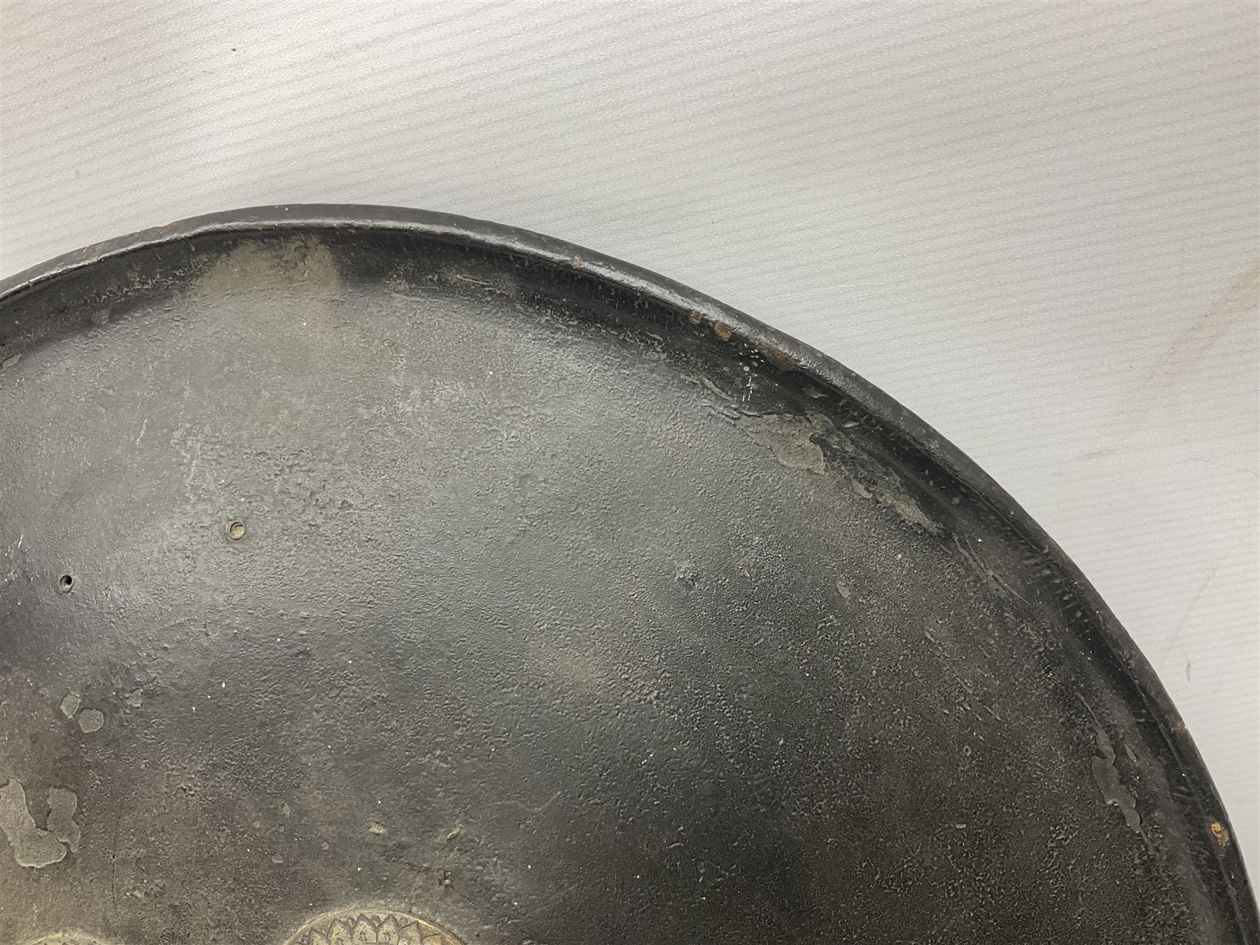 Indian black lacquered hide shield/dhal, of circular convex form with strongly outward-turned brim, fitted at its centre with four metal bosses, each of hemispherical form, with traces of silvered foliate decoration, the bosses corresponding on the inside with four iron rings for enarmes D49cm