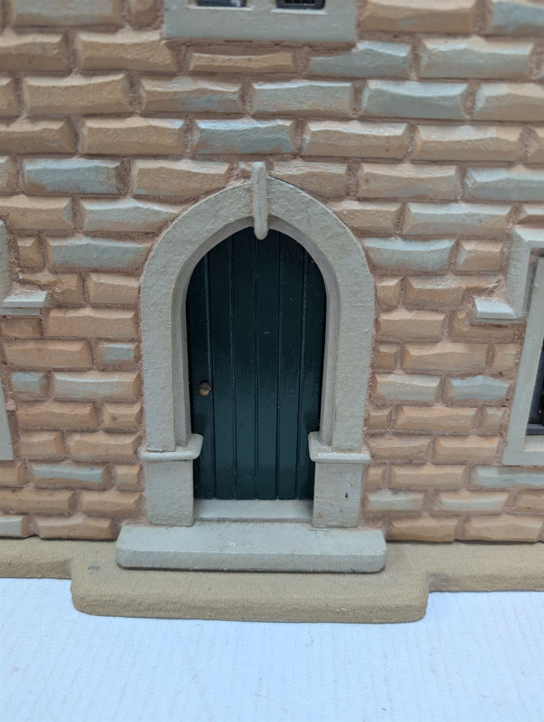 1:24 scale stone effect three-storey cottage dolls house, with green arched door and lattice effect windows, decorated to the interior with wooden floors, wired lighting and fire places, H45cm, W57cm, D26cm