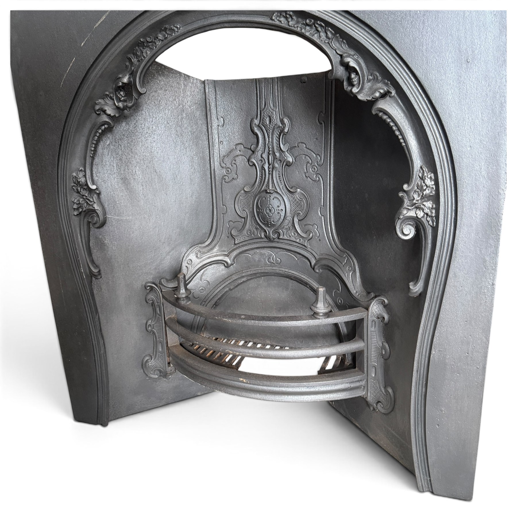Victorian cast iron fireplace, the arched surround cast with scrolling foliate ornament and central shield-shaped cartouche, fitted with a bowed fire basket, in black painted finish