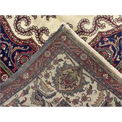 Northwest Persian signed Tabriz ivory ground carpet, central medallion with intricate floral motifs, the field and spandrels decorated with scrolling tendrils and palmettes, ivory main border with crimson and indigo floral decorations, surrounded by crimson guard bands