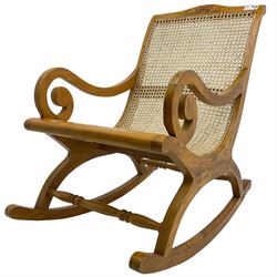 Late 20th century teak framed plantation style rocking chair, cresting rail carved with two elephants with upraised trunks, cane back and seat with scrolled arm terminals, rocker base united by turned stretcher