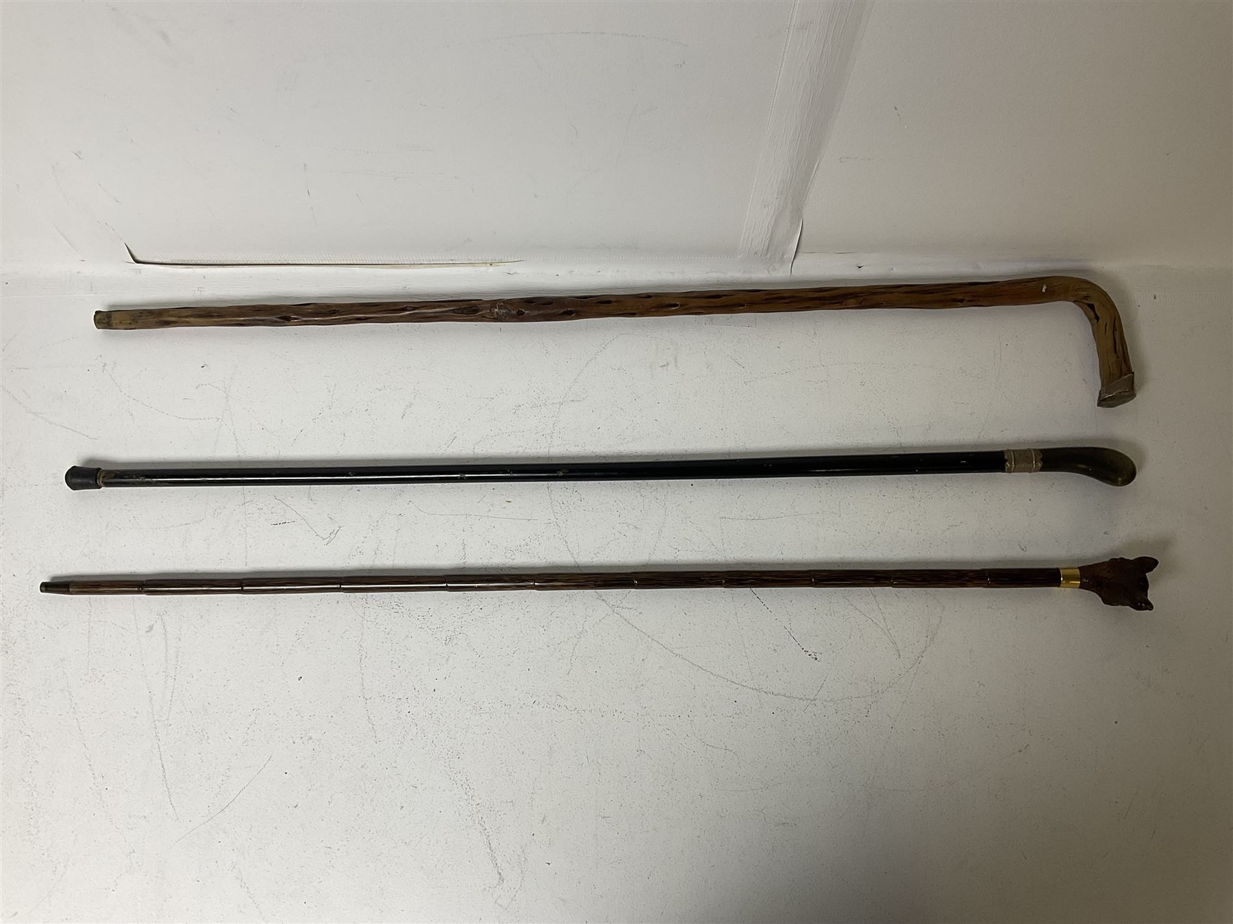 19th century painted bamboo walking cane, the handle carved as a fox with glass eyes, with gilt metal stamped LB, together with an ebonised wooden walking stick, with horn pommel and hallmarked silver collar and a curved wooden walking stick, with monogrammed white metal cap, tallest L90cm