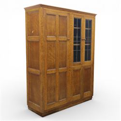 Edwardian oak glazed cabinet, moulded cornice above a panelled front and sides, fitted with lead glazed doors enclosing shelved interior, left side full length cupboard converted to enclose a gun cabinet, on a plain plinth base 