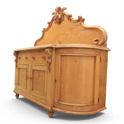 Victorian pine chiffonier, shaped moulded top with raised scroll carved back surmounted by carved fruit and foliate crest, fitted with two frieze drawers over two panelled cupboard doors, the outer cupboards of bowed form, carved foliate corbels, on plinth base