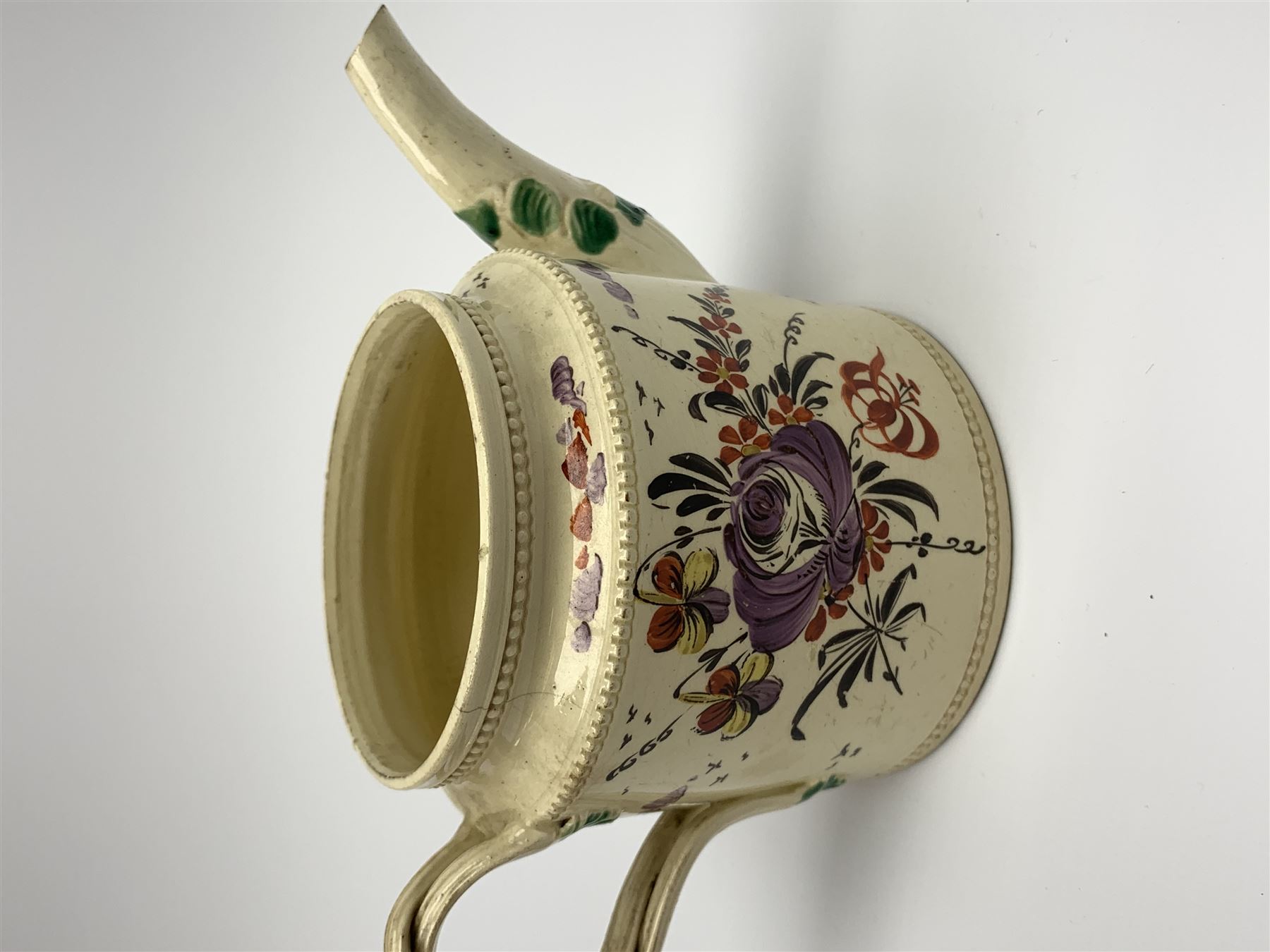 18th century creamware teapot, probably Leeds, with reeded entwined handle and floral finial to the cover, the body with hand painted polychrome decoration of figure to one side, and floral spray to the other, collectors paper label beneath inscribed Leeds Pottery, H11.5cm