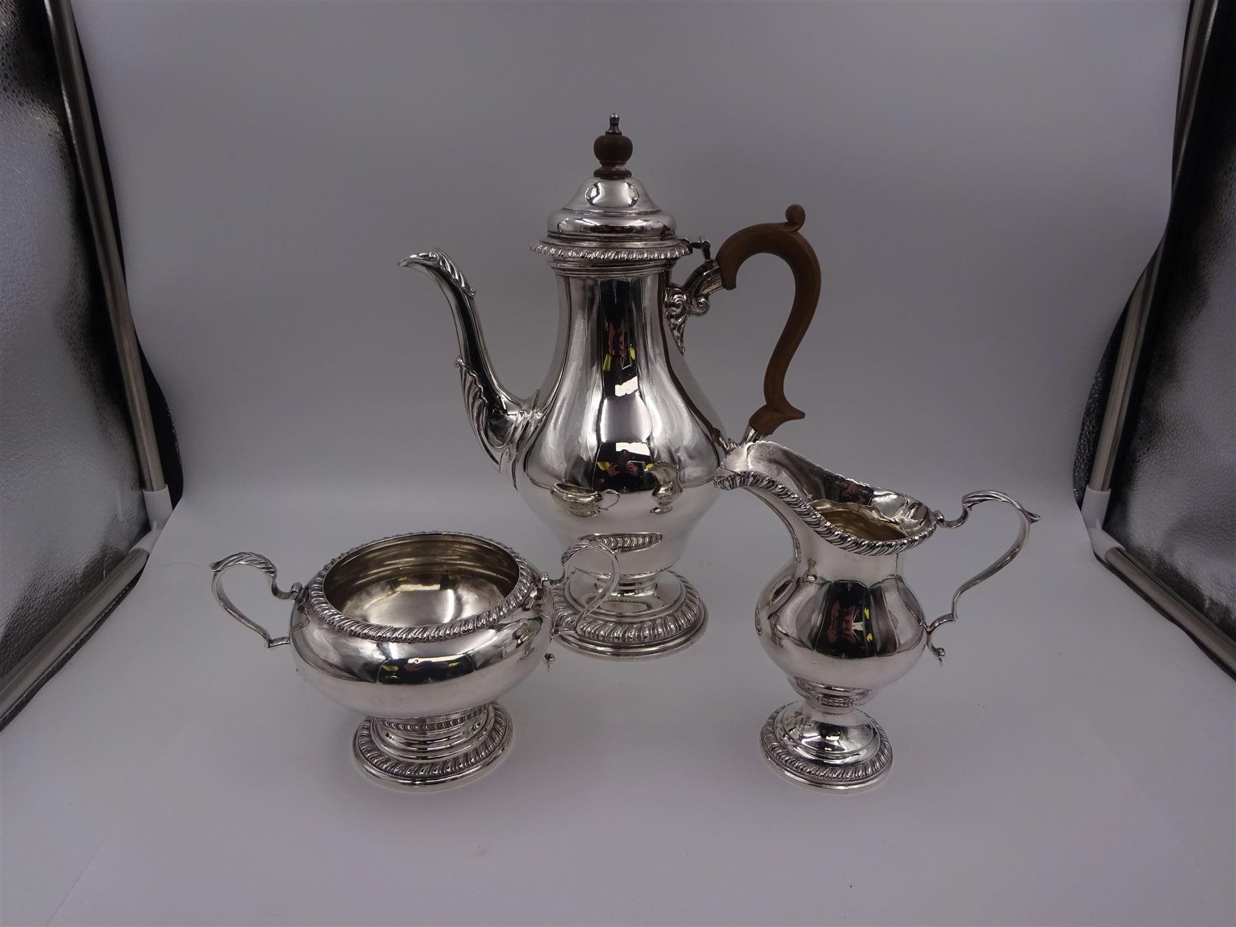 Mid 20th century three piece silver coffee service, comprising coffee pot, milk jug and twin handled open sucrier, of waisted form upon circular domed foot,  with oblique gadrooned rim, the milk jug and sucrier with acanthus capped handles, the coffee pot with wooden handle and finial, hallmarked William Comyns & Sons Ltd , London 1961, coffee pot H27.5cm
