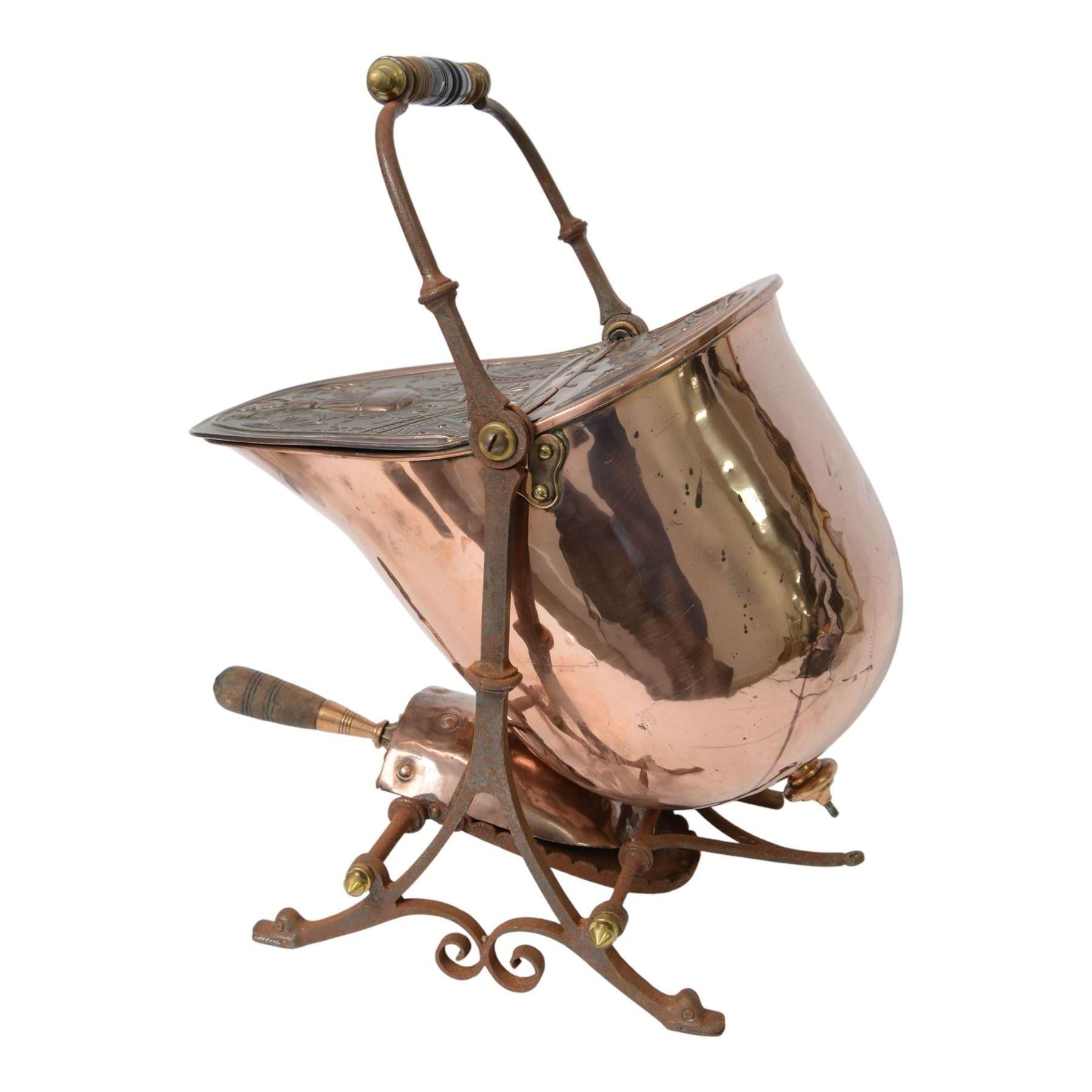 Victorian copper coal scuttle, the helmet shaped body tilting upon stand, with embossed hinged cover, turned wood handle and scoop H53cm
