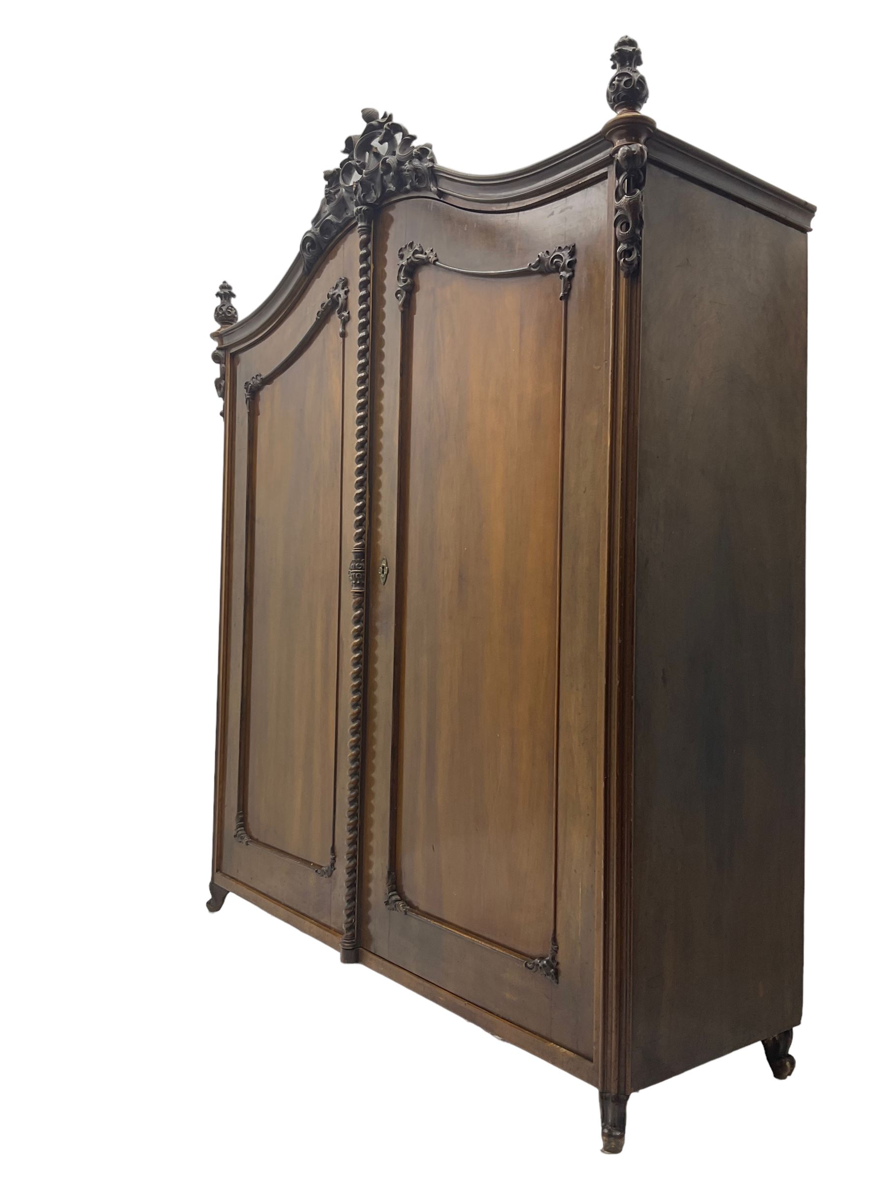 Early 20th century Italian walnut armoire wardrobe, the pierced and scrolling pediment carved with acanthus leaf detail, flanked by two scrolling cartouche with matching corbels below, the two panelled doors with applied carved rinceaux slips, with a central spiral turned upright, enclosing single shelf and hanging rail, raised on scroll feet