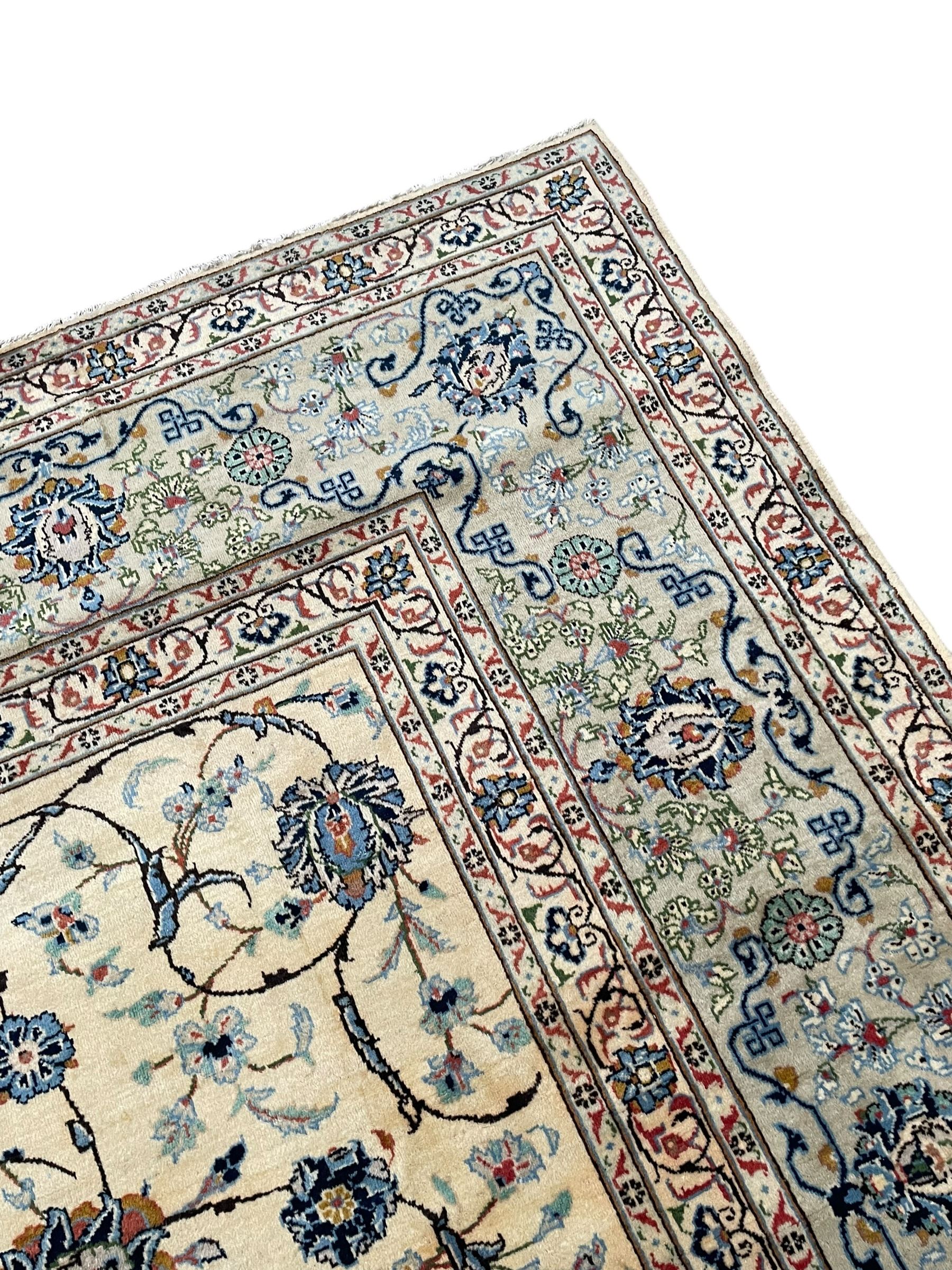 Persian Kashan ivory ground carpet, the field decorated with swirling foliate patterns and stylised plant motifs, scrolling border decorated with palmettes, within floral pattern guard stripes 