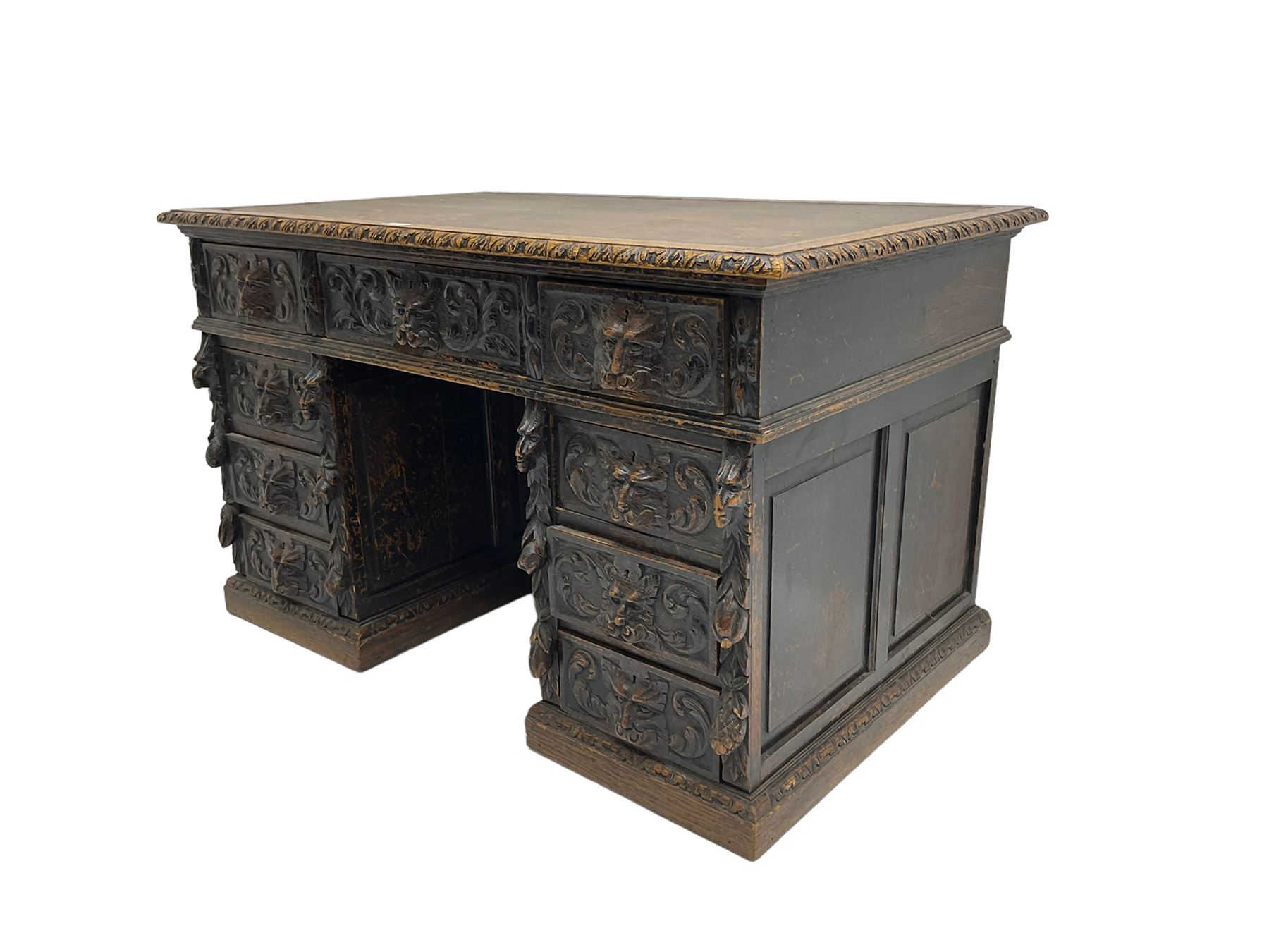Late 19th century Gothic revival carved oak twin pedestal desk, rectangular top with inset writing surface and carved edges, central frieze drawer flanked by eight drawers, all with green man carved handles and extending trailing foliage, carvings of pineapple and lion mask corbels, the pedestals with panelled sides and back, on plinth bases