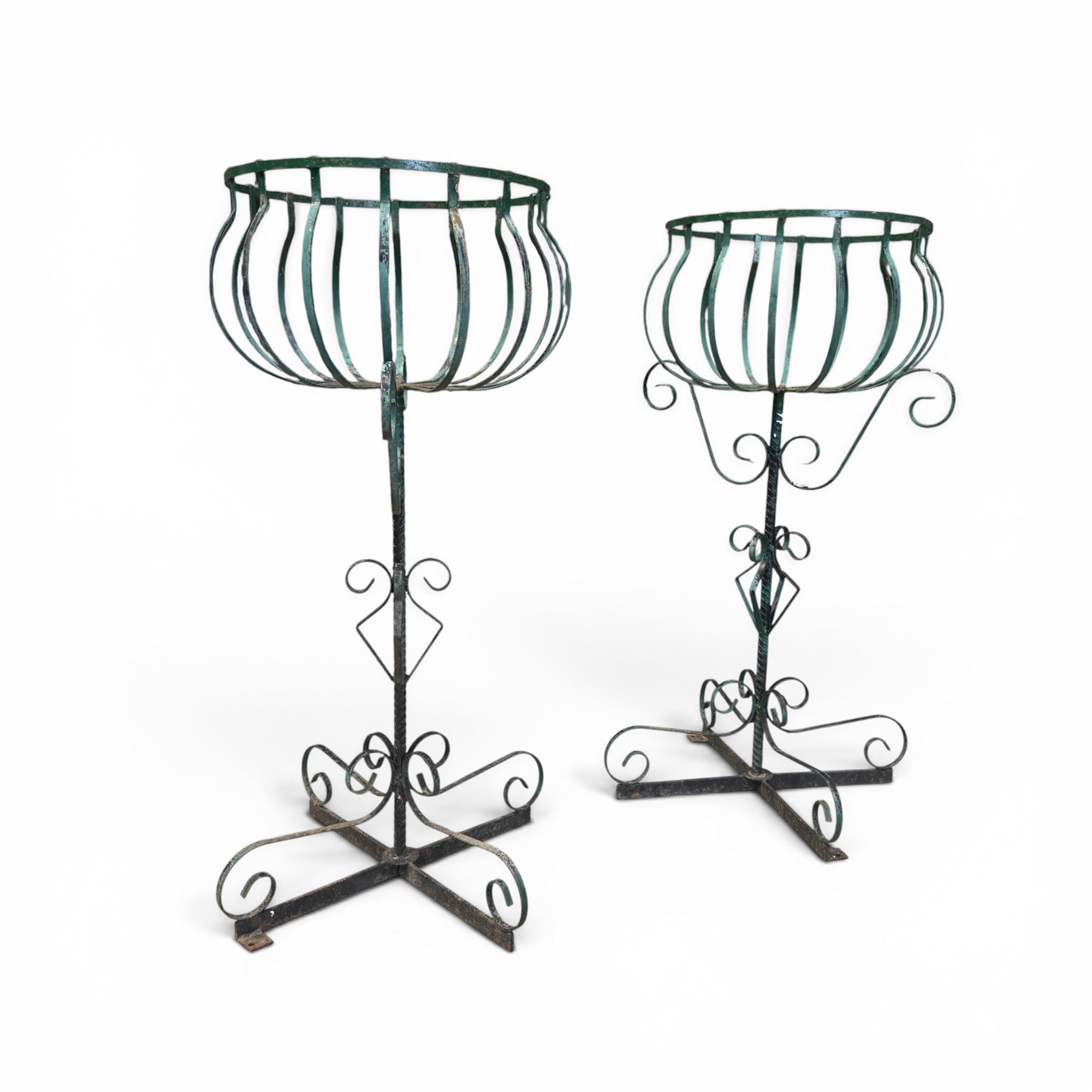 Matched pair of antique metal plant stands, each with circular strapwork basket tops, the scrollwork supports raised on an X-form base, in green painted finish with rustic patina