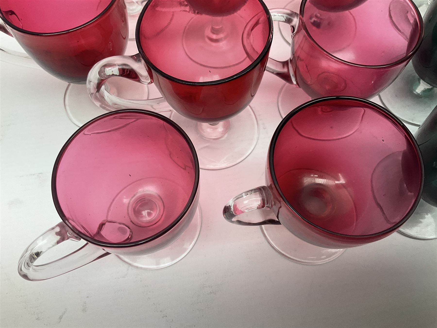 Collection of 19th century coloured glasses, to include nine cranberry glass punch cups, each with clear glass handle and foot and a set of six green glasses, with short clear stems, tallest H10cm