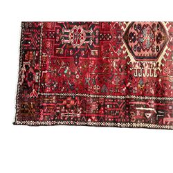 Persian Karajeh crimson ground runner rug, the field set with seven geometric lozenge medallions, the field decorated all over with stylised plant motifs, the banded border with repeating geometric shapes and patterns