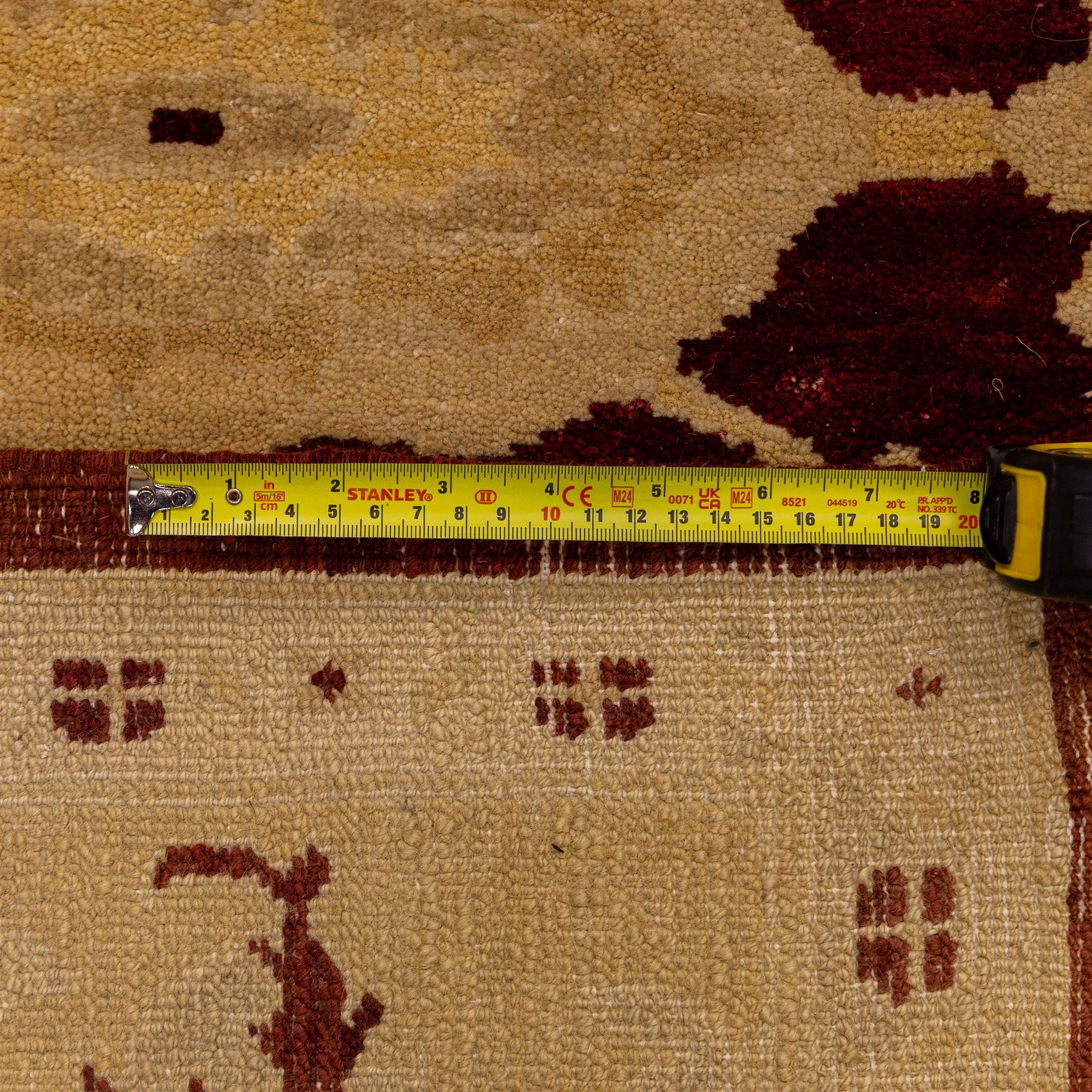 Ziegler design hand knotted wool rug, the rich red ground woven with oversized floral medallions and angular vine scrolls, framed by a contrasting ivory border of repeating floral ornament and minor guard stripes, with fringed ends