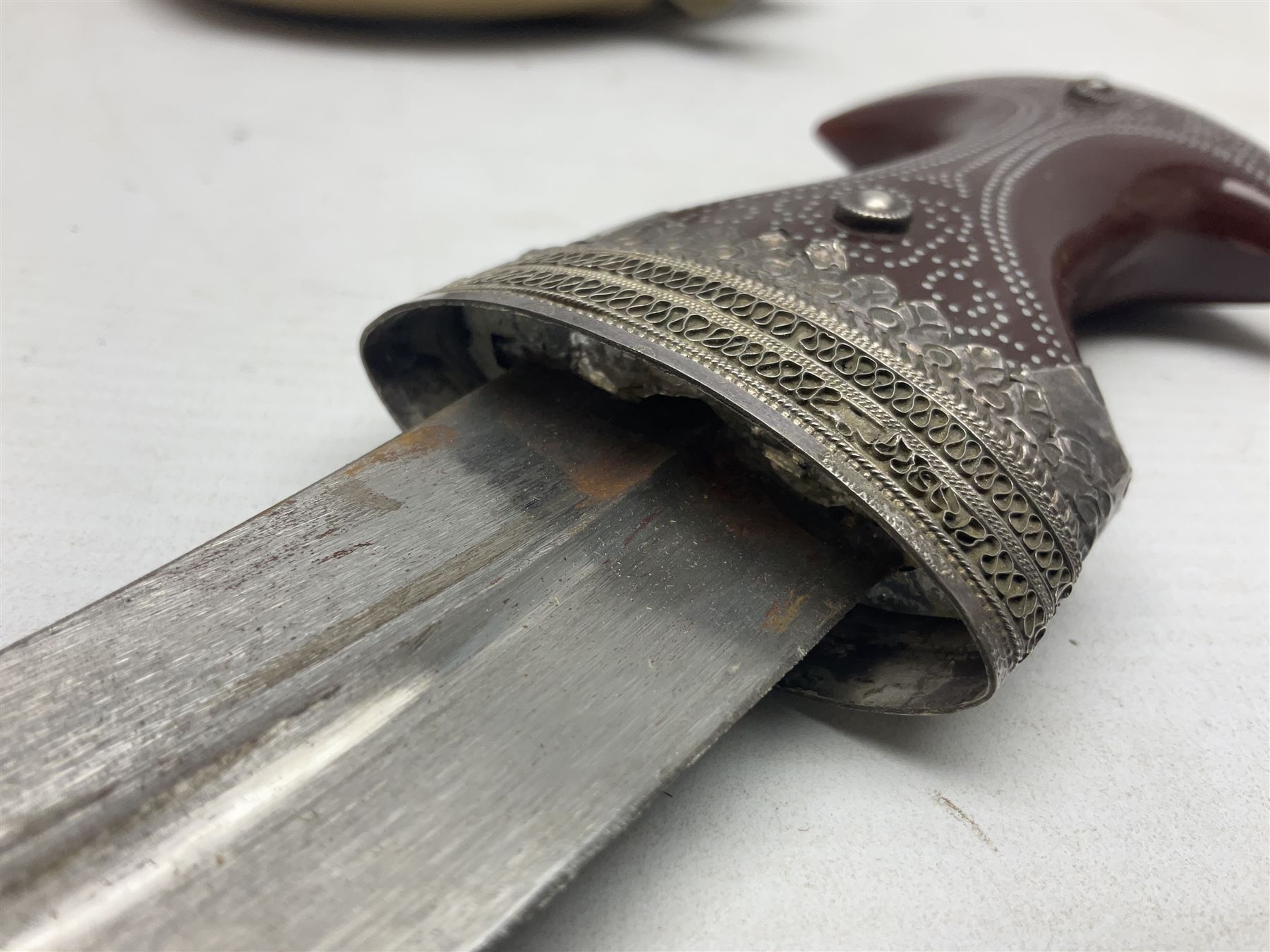 Omani Khanjar dagger, the 12.5cm curved blade with pronounced medial rib to either side, waisted horn style hilt with dome shaped pommel and inlaid pique work; in an intricately filigree decorated white metal scabbard with rings woven into the belt mount L25cm overall