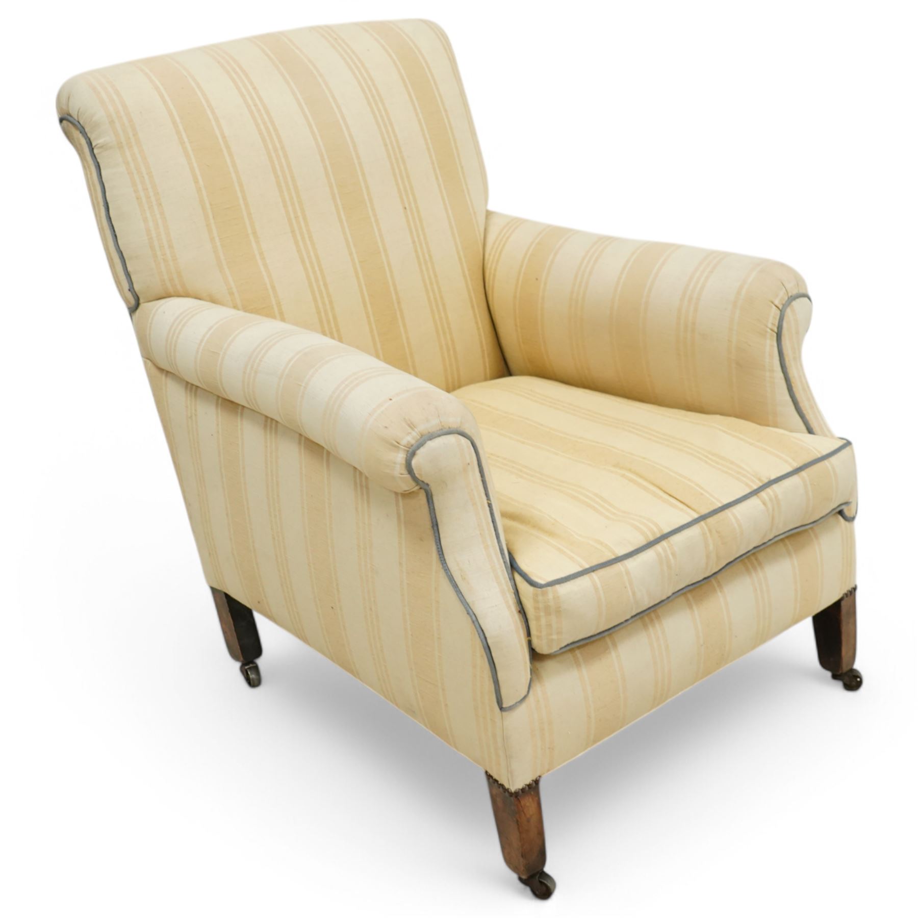 Early 20th century scroll arm armchair, upholstered in ivory striped cotton fabric with piped seams, sprung seat, on turned tapering front legs with brass caps and castors