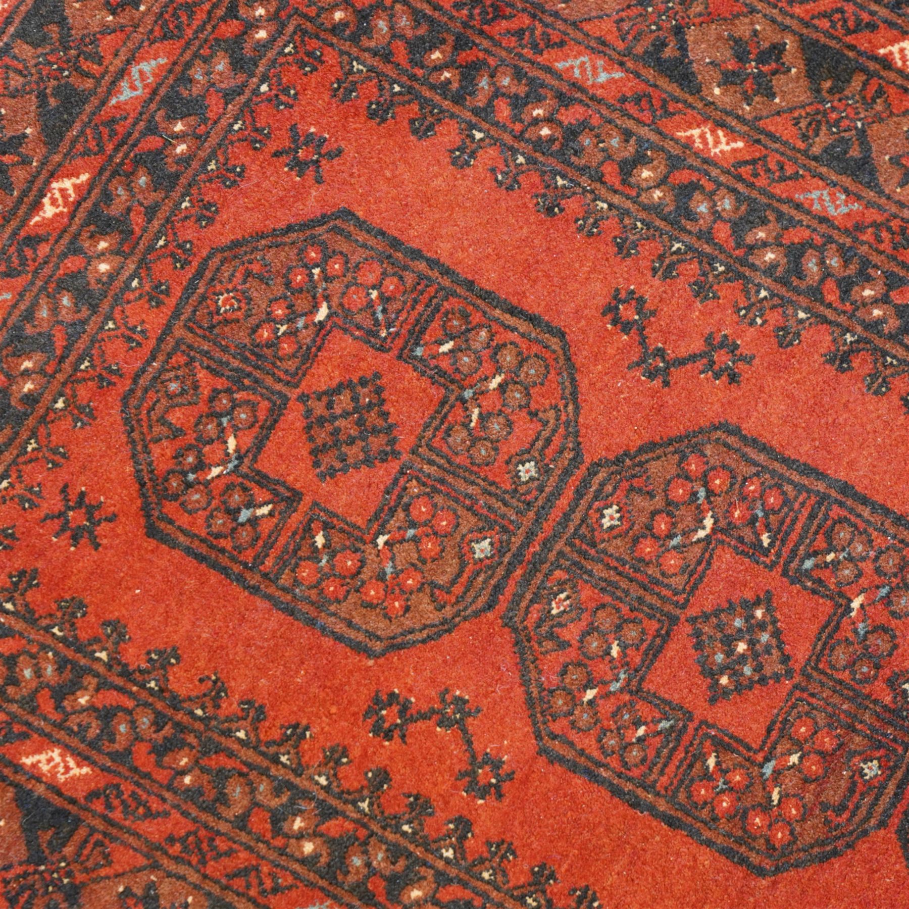 Bokhara red ground rug, the field decorated with three Gul motifs, within multiple borders with repeating geometric patterns (146cm x 103cm); together with an Afghan rug (144cm x 100cm)