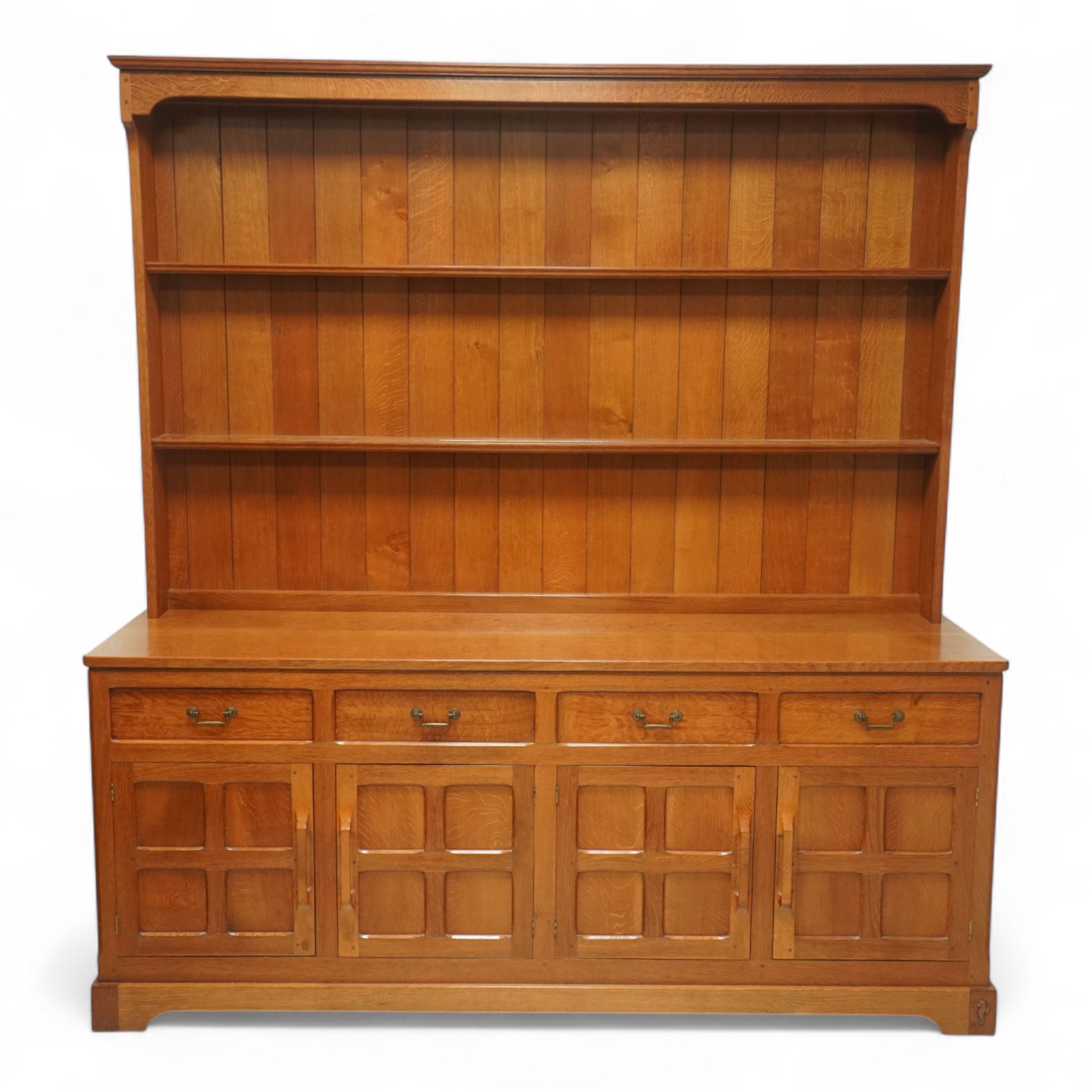 Seahorseman by Shaw & Riley - Yorkshire oak Welsh dresser, the dresser rack of rectilinear form with plain frieze and projecting moulded edge above two shelves with central shallow groove, the base section fitted with four drawers and a fitted cutlery drawer containing cutlery, above four panelled cupboard doors with geometric mouldings and carved sculpted handles, interior with single shelf and sides with geometric mouldings raised on a shallow plinth base with shaped bracket feet, with signature Seahorse carving from the workshop from the workshop of A. Shaw & Riley Ltd, Hessay