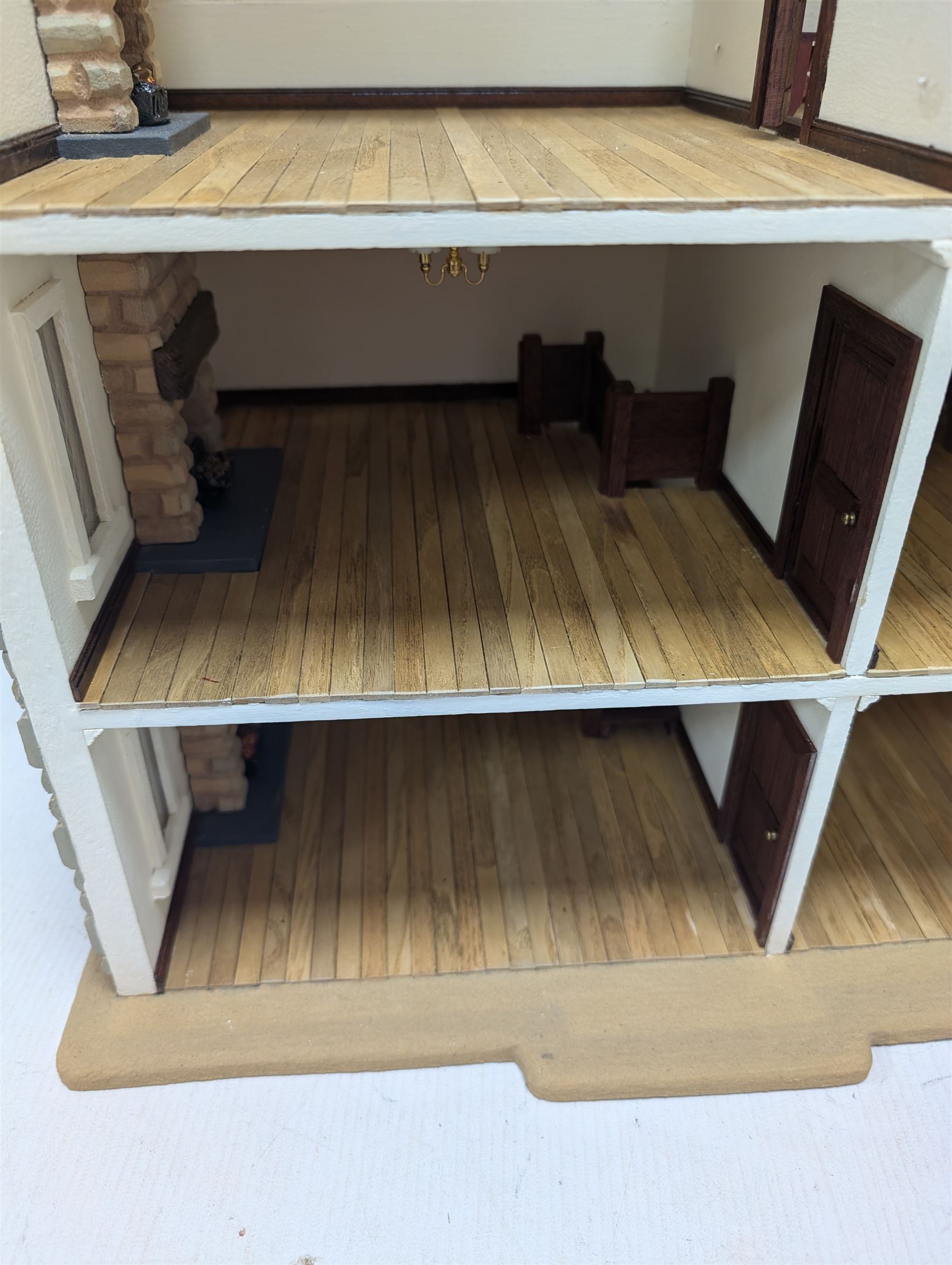 1:24 scale stone effect three-storey cottage dolls house, with green arched door and lattice effect windows, decorated to the interior with wooden floors, wired lighting and fire places, H45cm, W57cm, D26cm