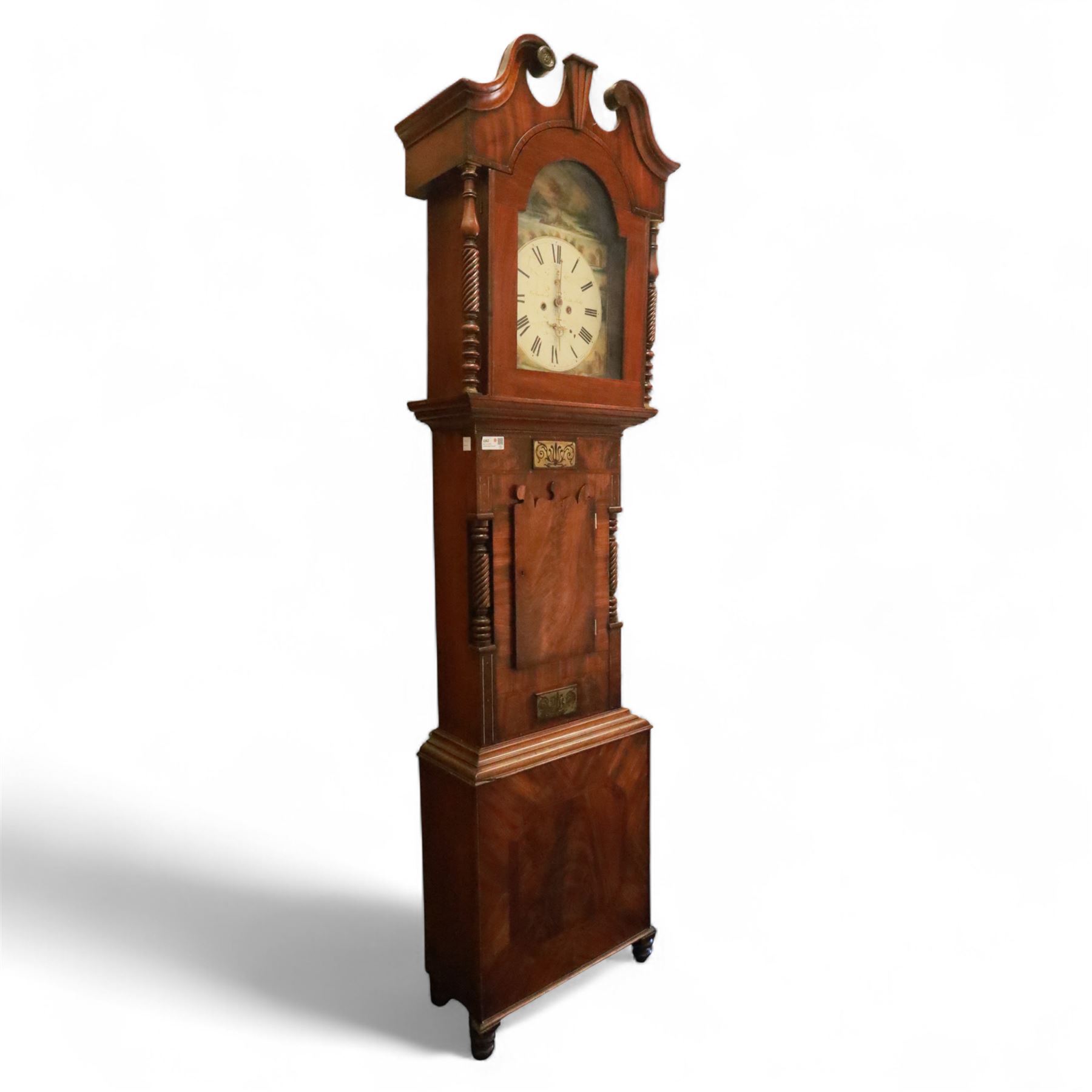 George Rutherford of Huddersfield- 8-day mahogany longcase clock c1880, with a swan neck pediment and turned patera, hood with shaped back splats and a break arch hood door flanked by ring turned pilasters, trunk with conforming recessed pilasters and a short wavy-topped trunk door, on a broad plinth raised on bracket feet, fully painted dial with matching pastoral depictions to the spandrels and break arch, with makers name, Roman numerals, subsidiary seconds and date dials and matching stamped brass hands, dial pinned via a falseplate to a rack striking movement striking the hours on a bell (bell missing). With pendulum, no weights.