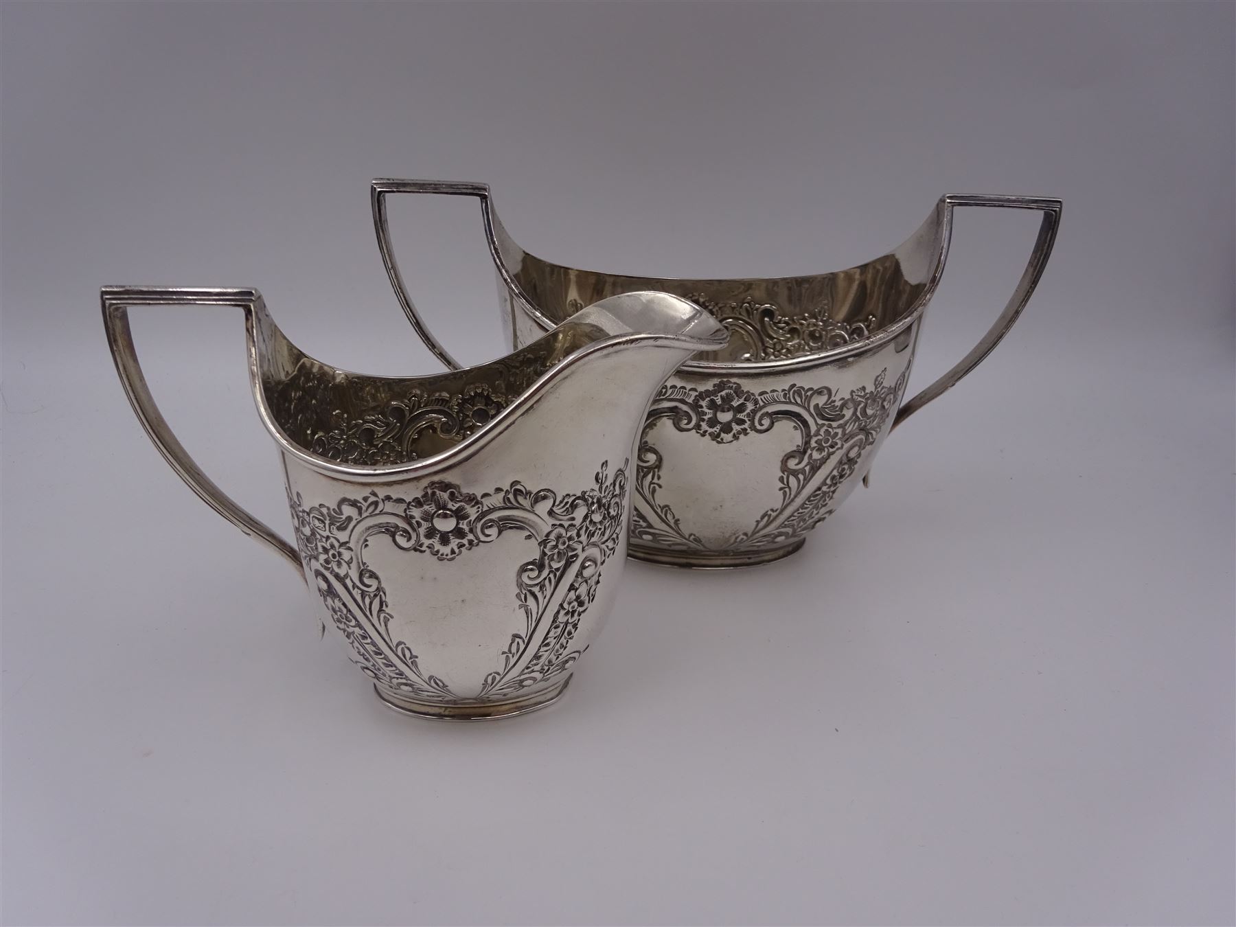 Late Victorian silver milk jug and twin handled open sucrier, each of oval form with angular handles and embossed floral, foliate and C scroll decoration, hallmarked James Deakin & Sons, Sheffield 1899, sucrier with handles H10.8cm