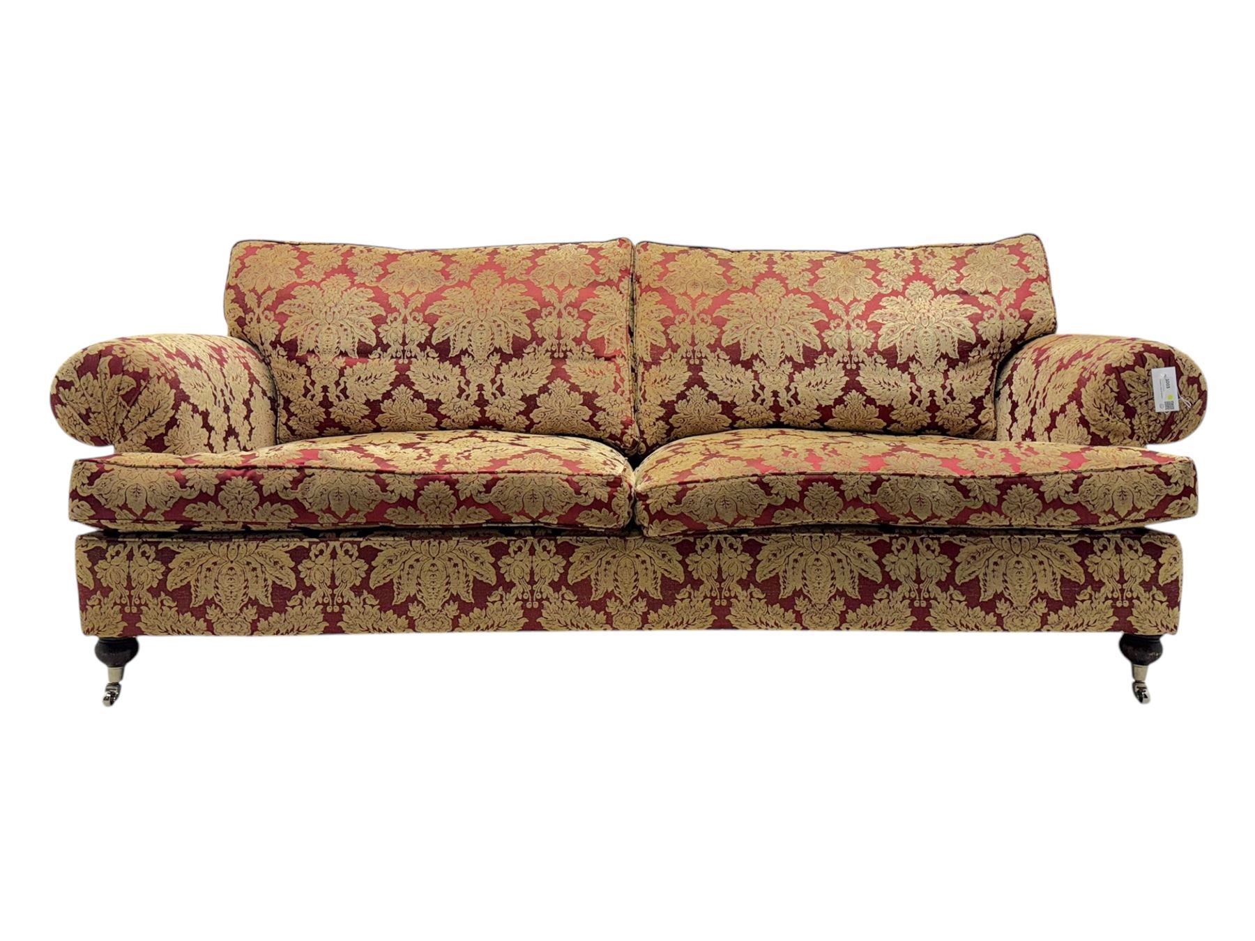 Duresta - pair of Grande three-seat sofas, traditional shaped with rolled arms and upholstered loose cushions, in red ground fabric with raised gold foliate pattern, on turned feet with brass castors 