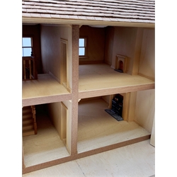 A 24th scale wooden model of a house, or dolls house, with 'tiled' roof, sash windows, and two bay windows to the hinged front, opening to reveal four rooms and two hallways, detailed with kitchen stove and fireplaces, H45cm L54cm D36cm. 
