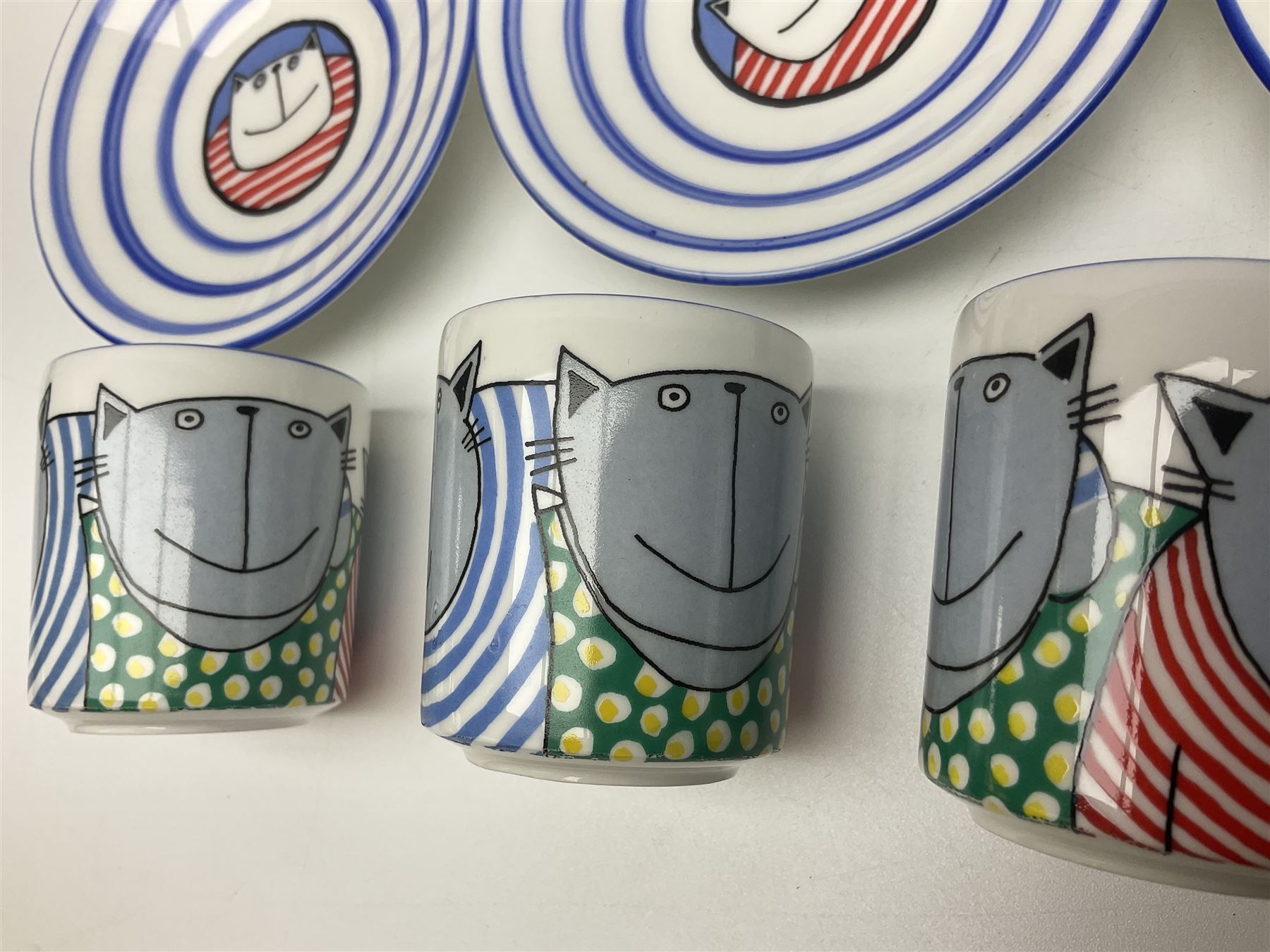Modern studio pottery by Josie Firmin, to include cup and saucer, three espresso cups and saucers, pair of egg cups etc, each hand painted with varying cartoon cat designs