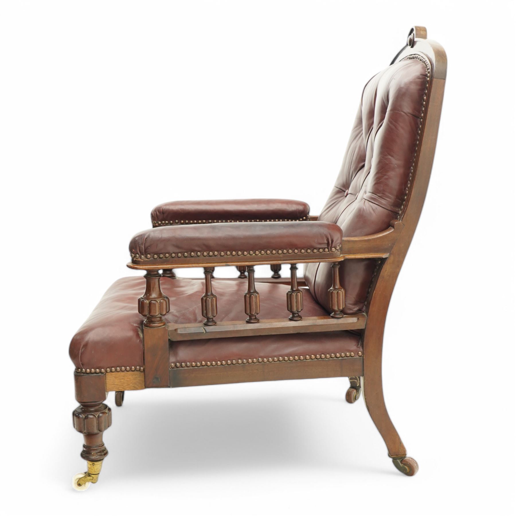 Late Victorian mahogany open armchair, arched cresting rail decorated with turned roundel, upholstered in buttoned burgundy leather, the upholstered arms on turned and lobe carved balustrade, turned and lobe carved front feet with brass and ceramic castors 