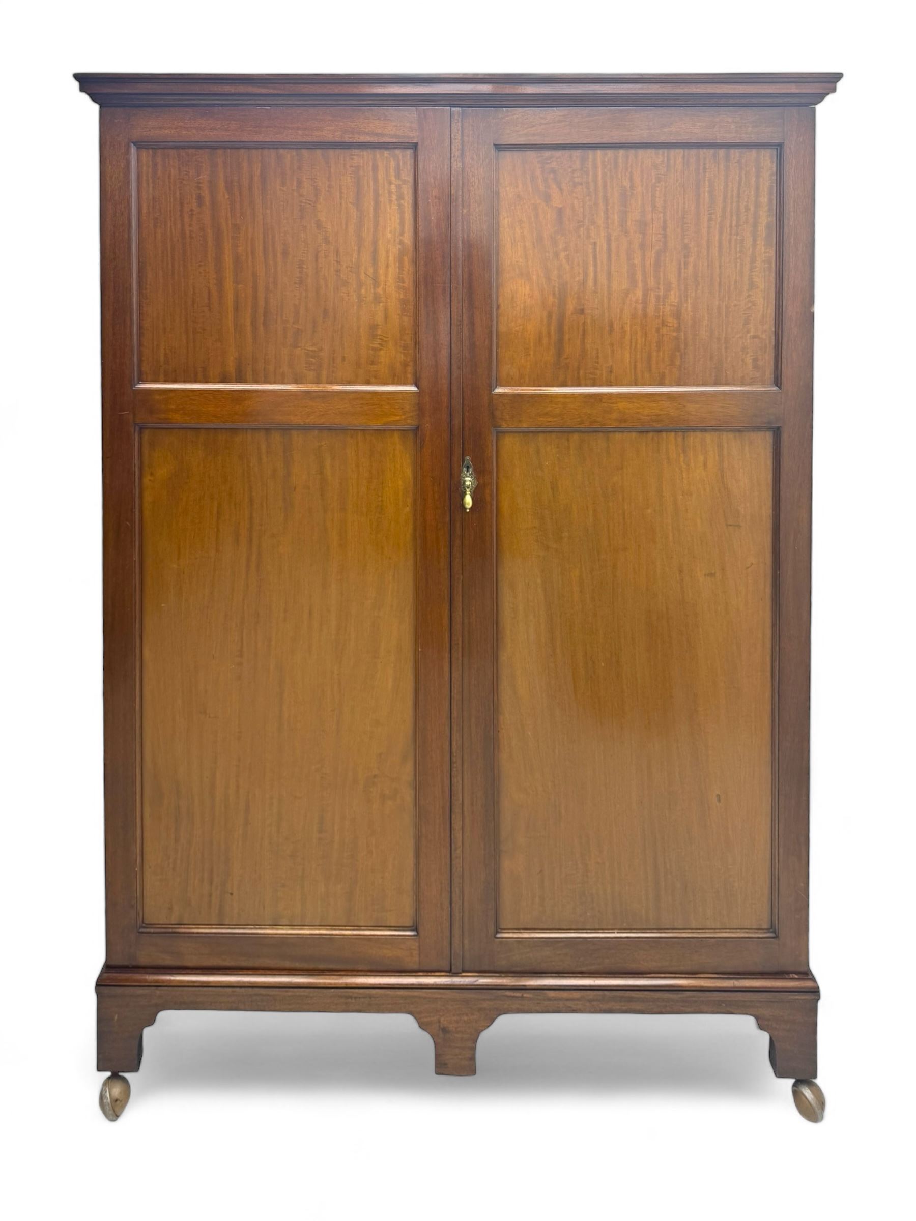 Wylie & Lochhead, Glasgow - early 20th century mahogany and satinwood double wardrobe, projecting cornice over panelled doors, interior fitted with mirrored door, shelves, drawers, hooks and hanging rail, raised on bracket supports with ceramic castors