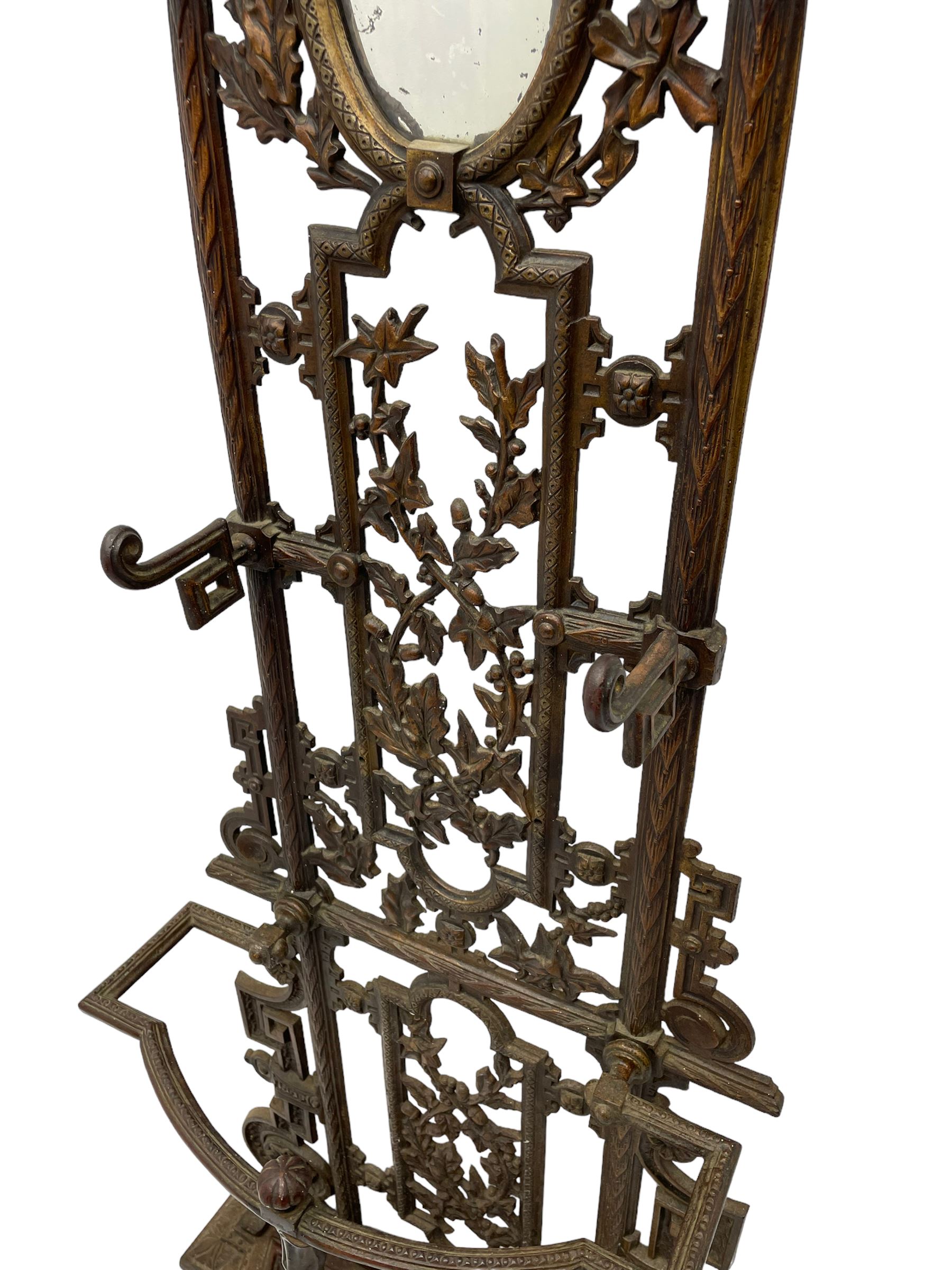 19th century cast iron hallway hat and coat stand, the arched frame decorated with overlapping foliage, central oval mirror surrounded by trailing oak leaves and acorns, with extending umbrella and stick stand, the curved plinth base decorated with acanthus leaves, with impressed and mounted R.d. lozenges