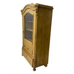 Late 19th century Continental pine vitrine, shaped and moulded arched cornice over a single glazed door enclosing adjustable shelves, flanked by carved pilasters with foliate and geometric motifs, fitted with single moulded drawer, raised on compressed bun feet