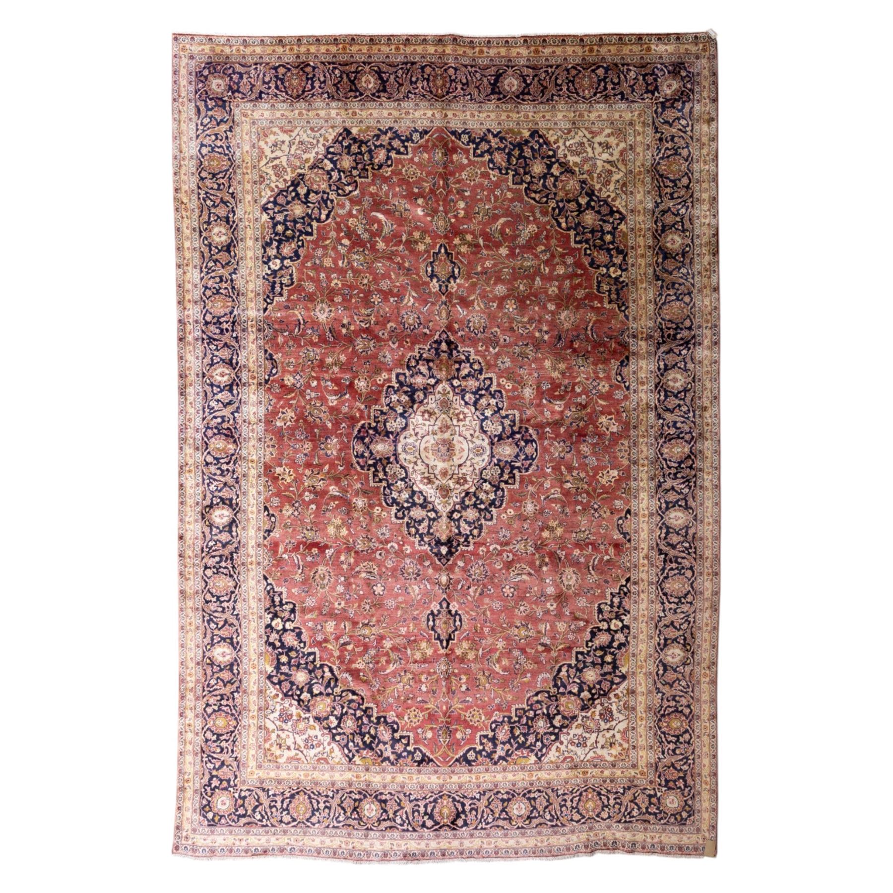 Large Central Persian Kashan hand-knotted carpet, madder red field with central cusped medallion on beige ground enclosed by indigo border with an intricate all-over arrangement of scrolling vines and floral motifs within conforming spandrels and a indigo ground main border ornamented with floral designs, enclosed by guard stripes and cotton fringe ends 