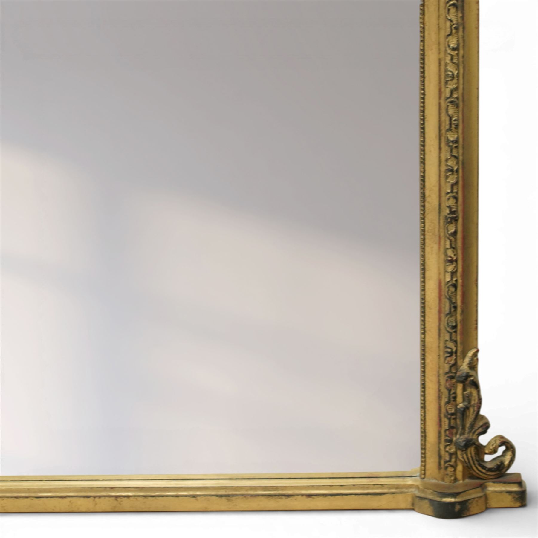 Regency style gilt overmantle mirror, arched rectangular frame with moulded surround, surmounted by a central anthemion and scrolling foliate crest, the frame enriched with beaded and foliate mouldings, the lower corners with applied scroll terminals, enclosing a single rectangular mirror plate