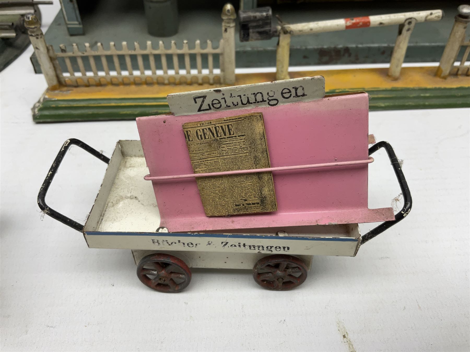 '0' gauge - Bing tin-plate two-storey double sided station with open walk-through to one end, rail side canopy, hinged doors and removable roof giving access to clock illumination L35cm; Bing hand-cranked turntable and open wagon; Marklin tin-plate level crossing barrier and Newspaper vendor's tin-plate four-wheel hand cart (5)