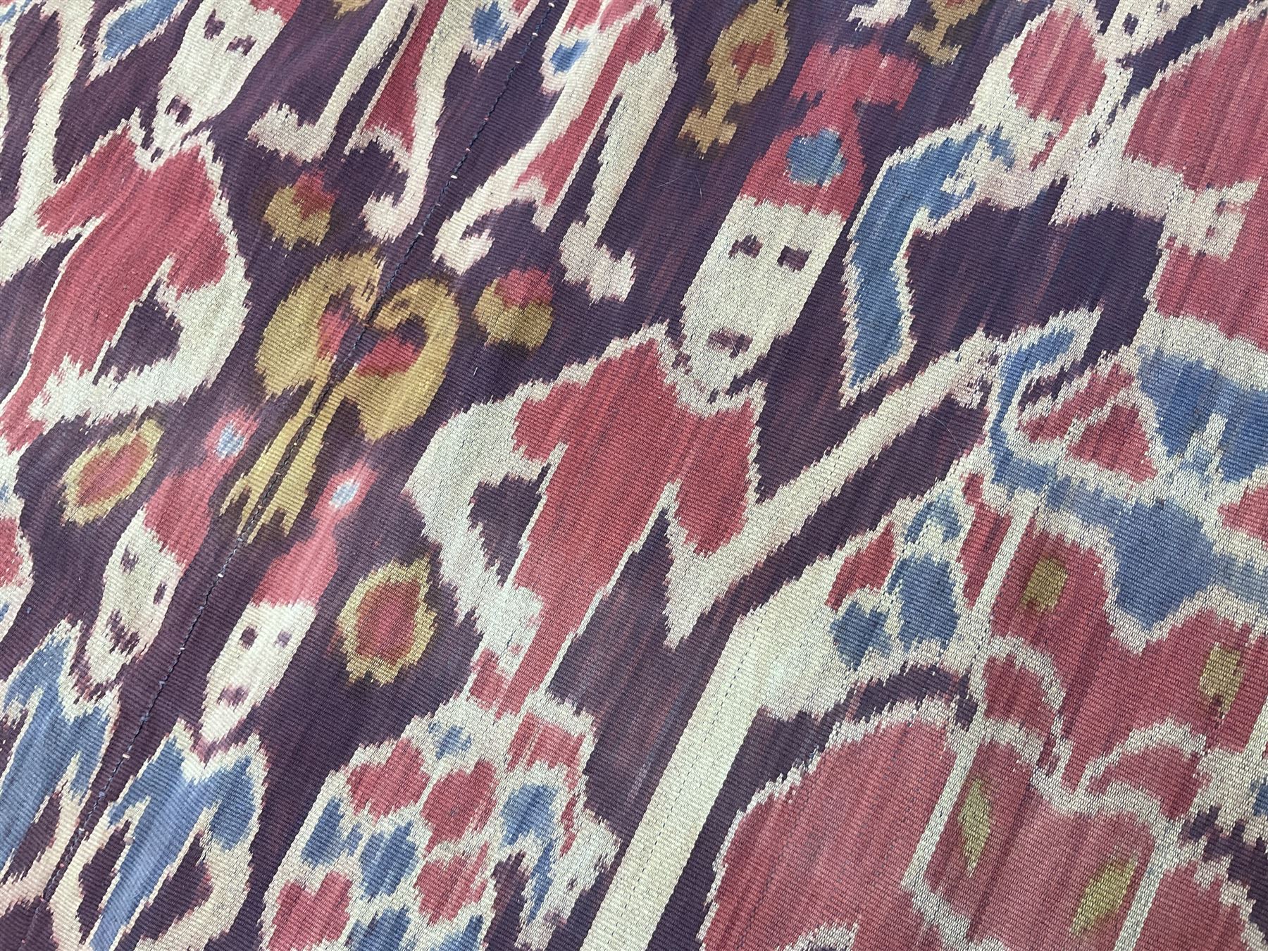 Ikat Man’s Cloth (Hinggi Kombu), East Sumba, Indonesia, woven in red, blue and yellow-brown warp ikat, constructed of two mirroring long panels, the motifs arranged in four bands depicting warrior figures astride rearing horses, high-ranking figures and guardians within geometric borders, on carved wooden wall hanger, L295cm
