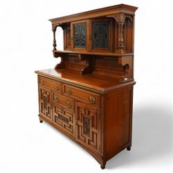 Early 20th century golden oak dresser sideboard, superstructure with three stained and leaded glass doors flanked by carved uprights above an open display shelf, the base with three drawers and geometric panelled cupboard doors, enclosing drawers with cutlery and bottle compartments, raised on short feet