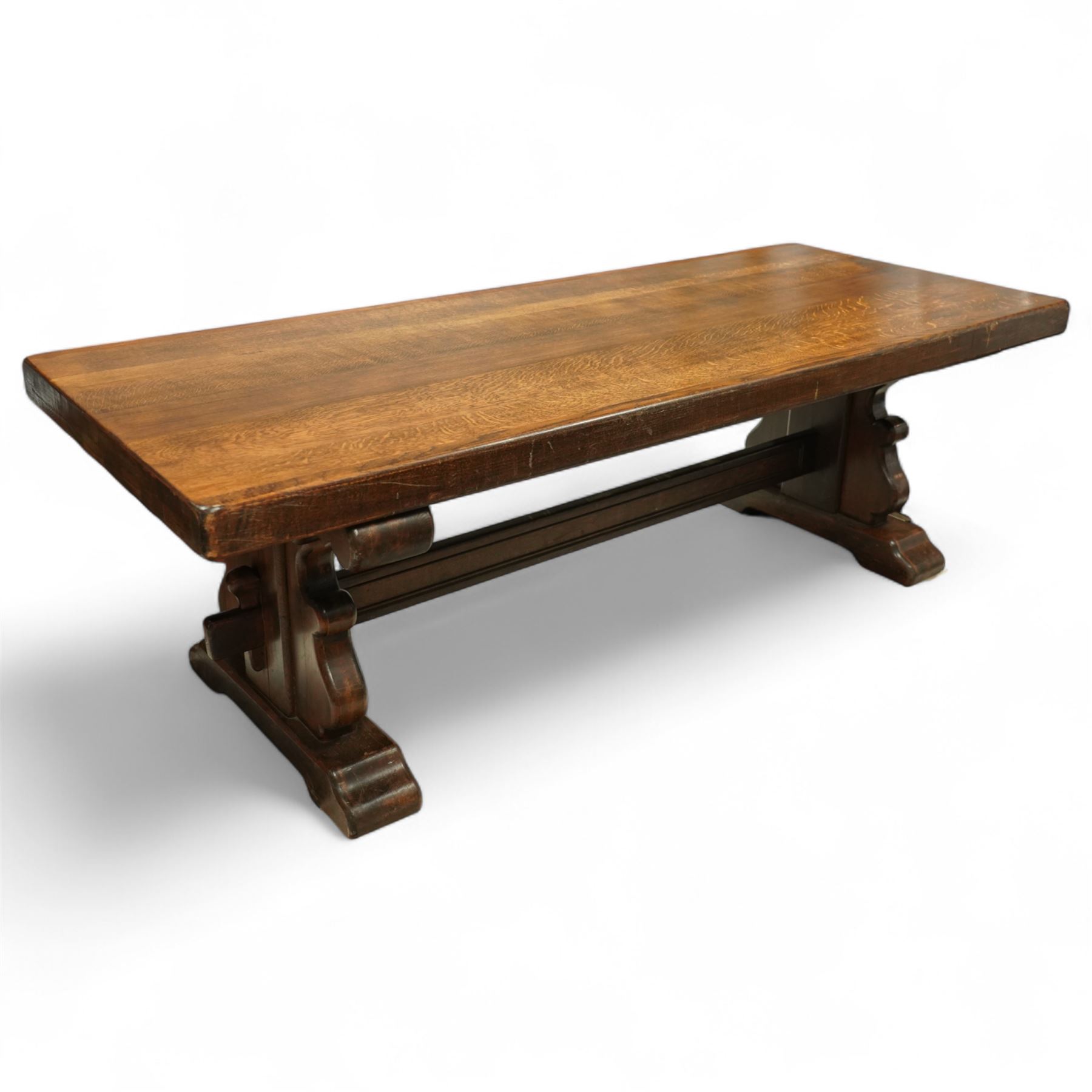 Early 20th century French oak refectory table, the thick rectangular top with cleated ends above shaped lyre-form trestle supports, united by a central stretcher, on broad scrolled feet, displaying well-figured quarter sawn grain across the top