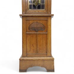 German-Art Deco 8-day longcase clock in an oak case, with a curved top and open fence work pediment, with reeded decoration and a fully glazed case door with a rectangular brass open work panel, on a tall rectangular plinth with a period  carved motif, circular slivered dial with Arabic numerals and spade hands, two train HAC (Hamburg and American Clock Company) weight driven movement, sounding the hours and half-hours on a coiled gong, with weights and pendulum.   